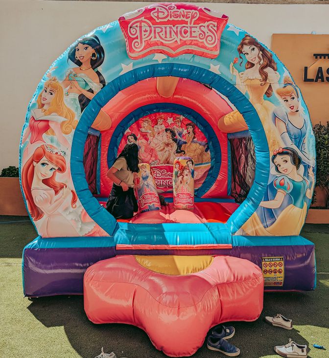 Princess-themed inflatable bounce house with pink and blue arches and cartoon characters in an outdoor area