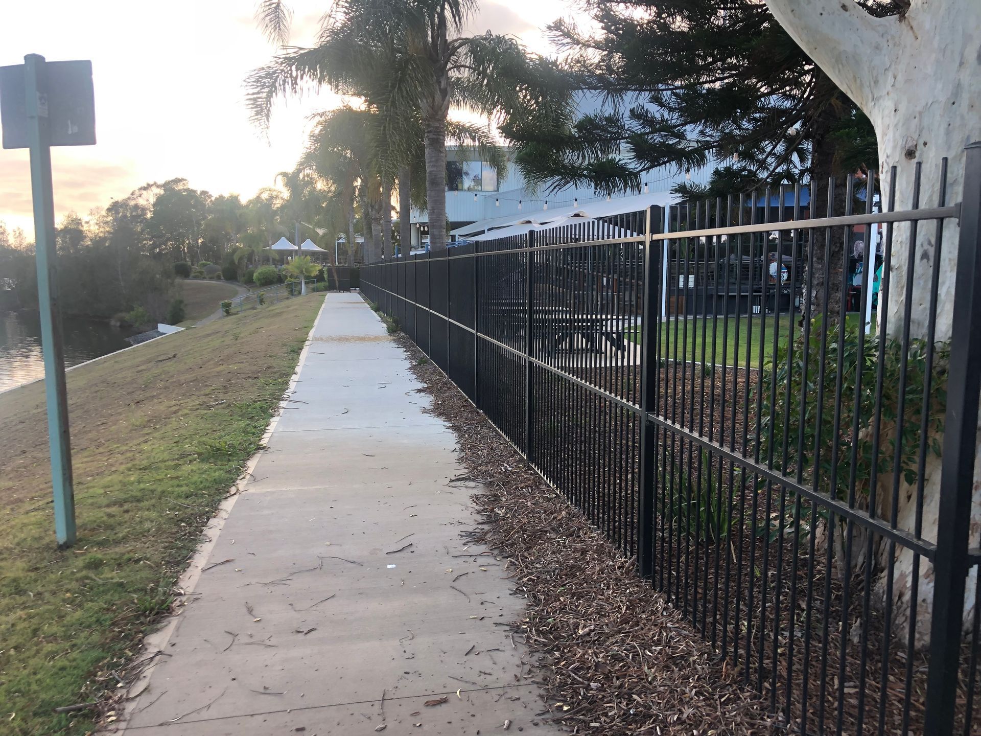 A Paved Path Next to a Black Fence, With a Grassy Bank and Trees in the Background — Fencer Steve In Kempsey, NSW