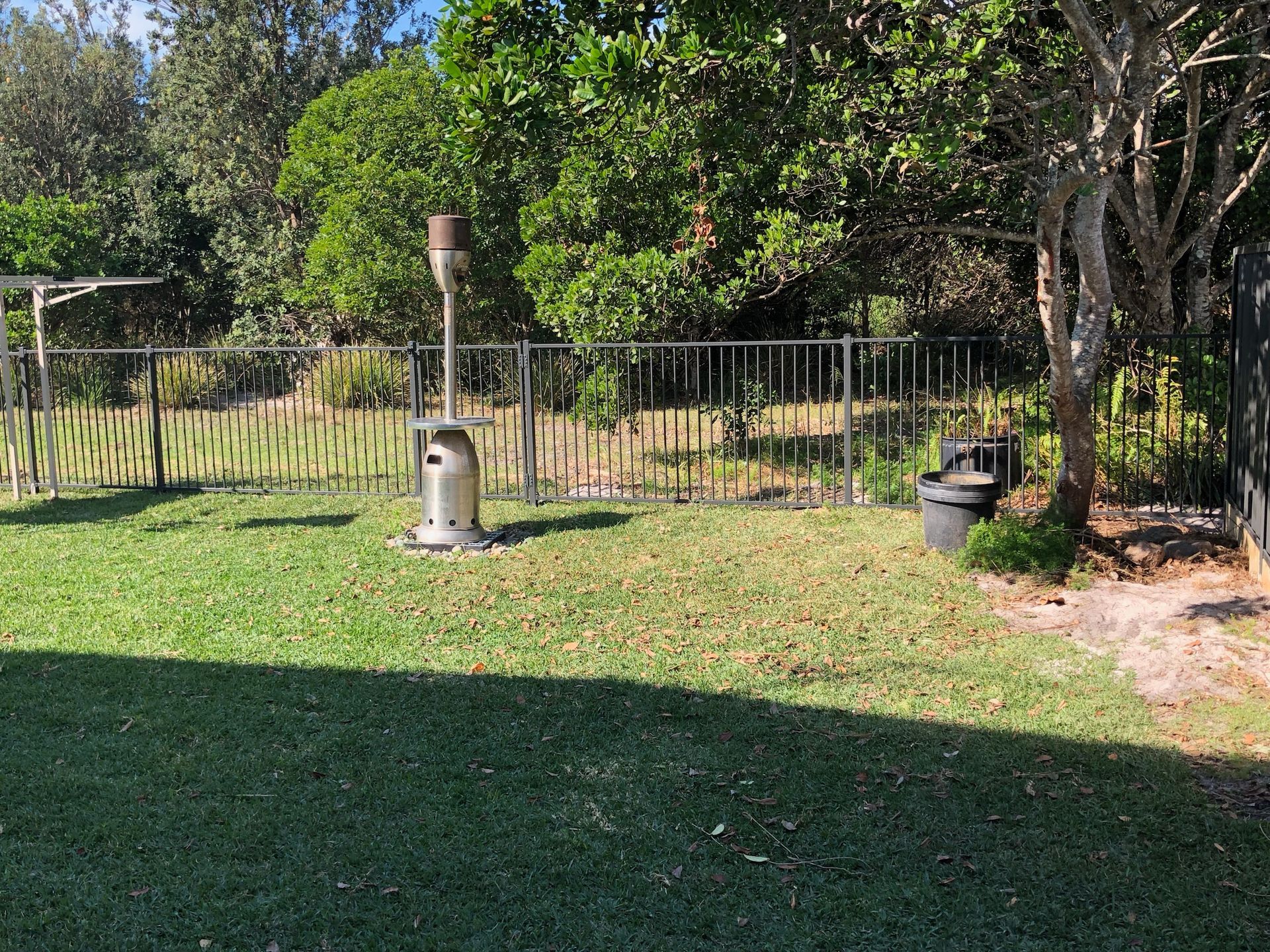 Lawn in a backyard with a heater, fence, and trees on a sunny day — Fencer Steve In Temagog, NSW