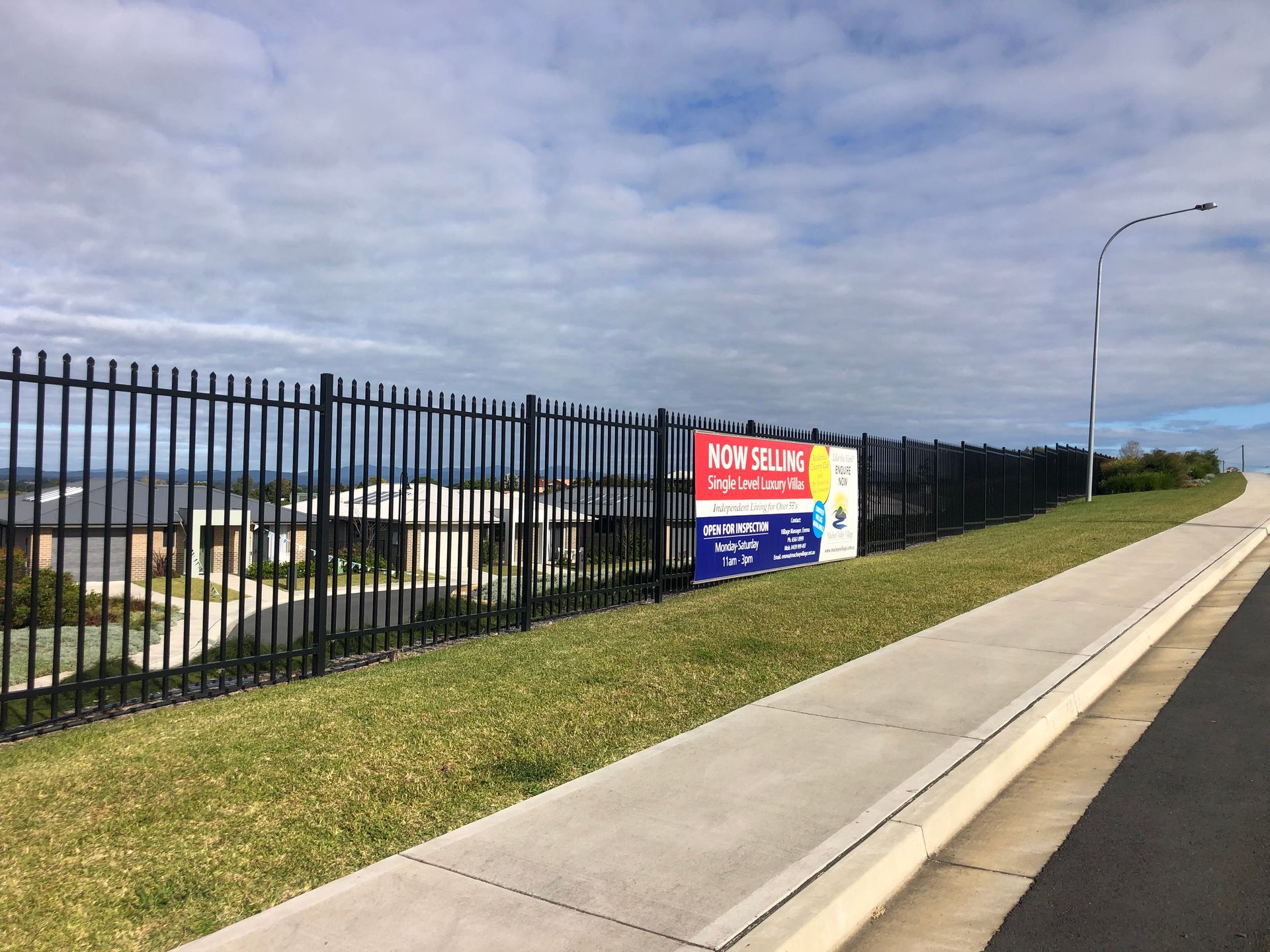 Black fence with for sale signs overlooking suburban homes under a cloudy sky — Fencer Steve In Temagog, NSW