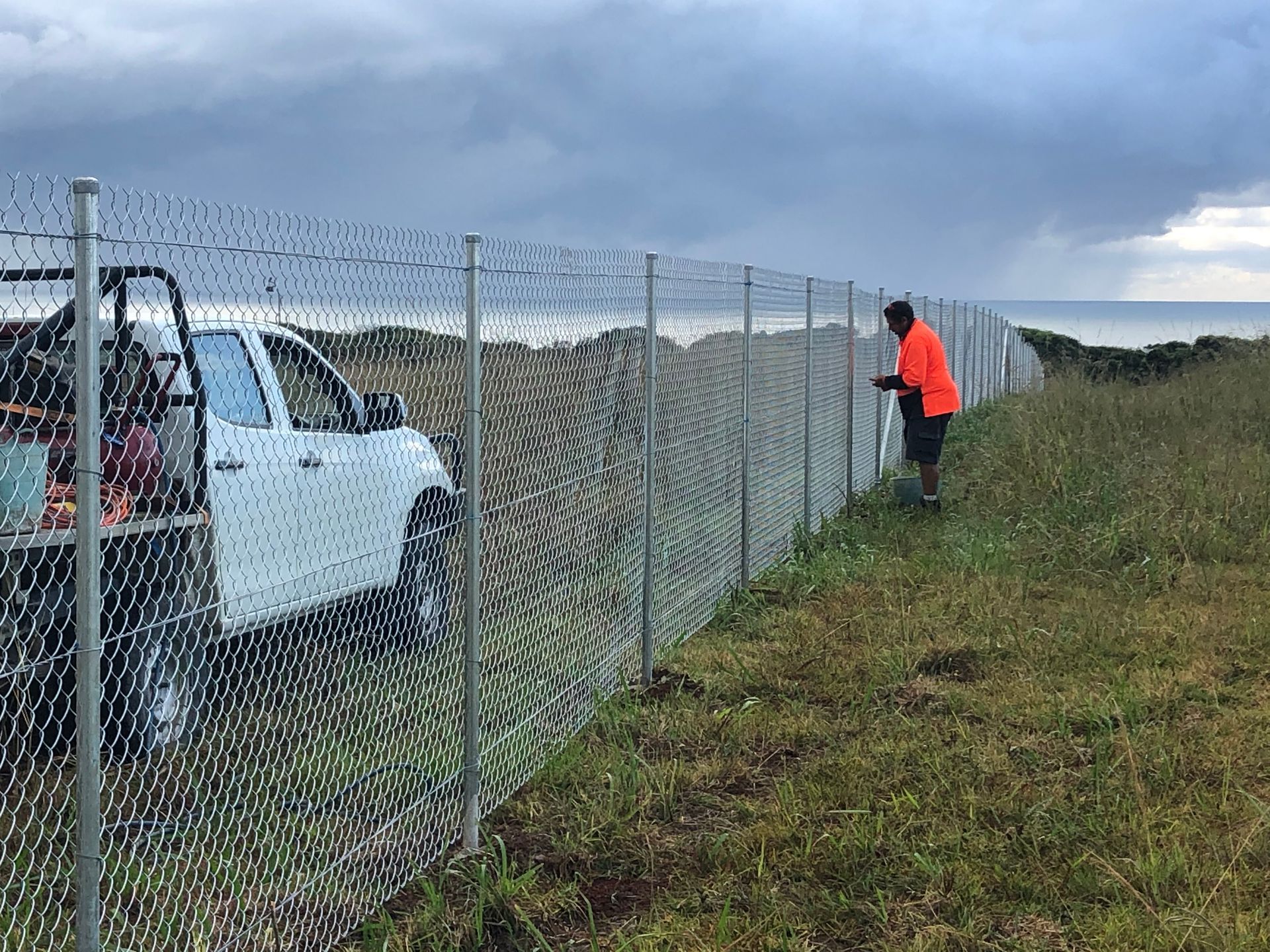 Man in Orange Vest Inspects Chain Link Fence Beside a White Truck — Fencer Steve In Temagog, NSW