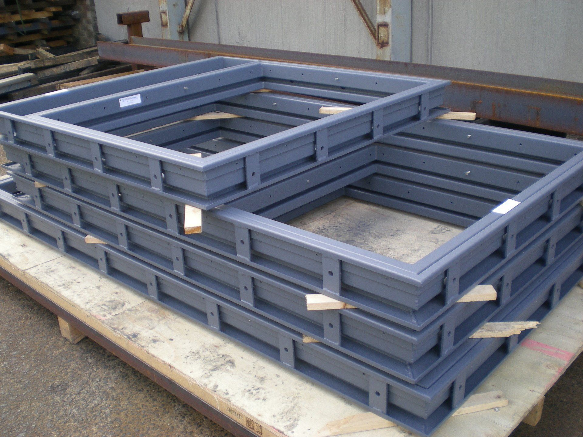 Stack of gray metal rectangular frames with central cutouts, likely for construction or building. 