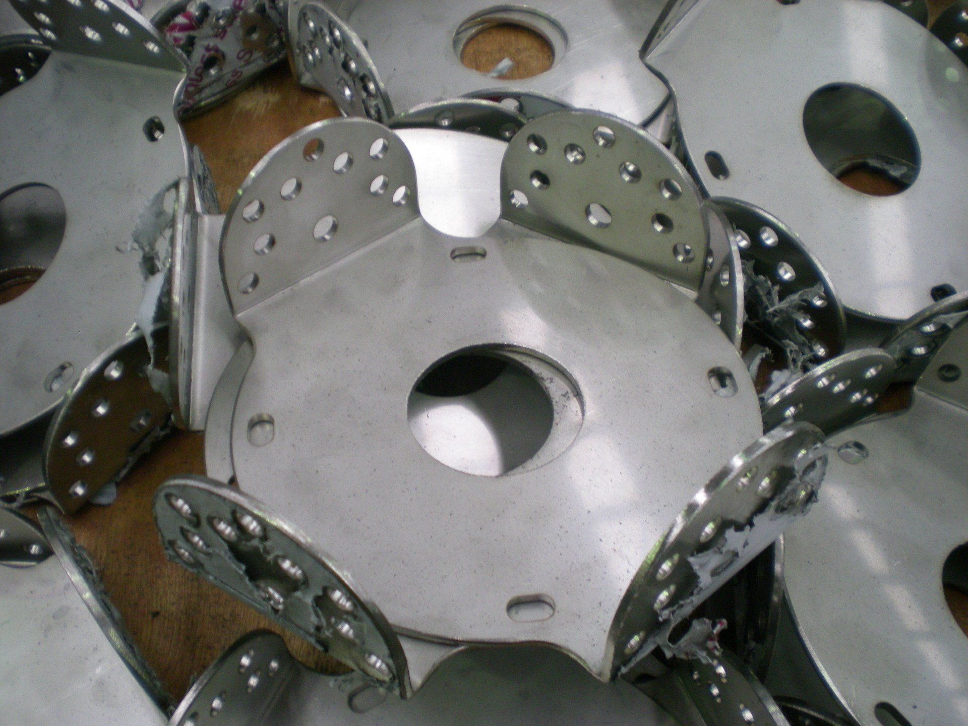 Pile of shiny, silver metal disks with a central hole and attached petal-like extensions.