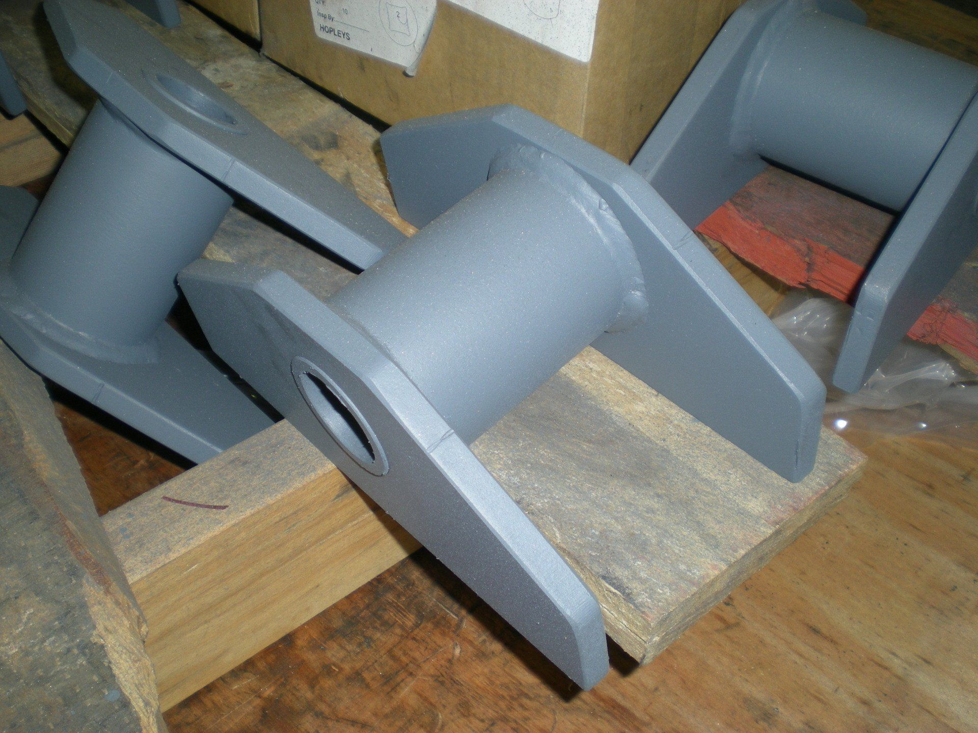 Several gray metal brackets resting on wooden blocks, likely manufactured parts. 