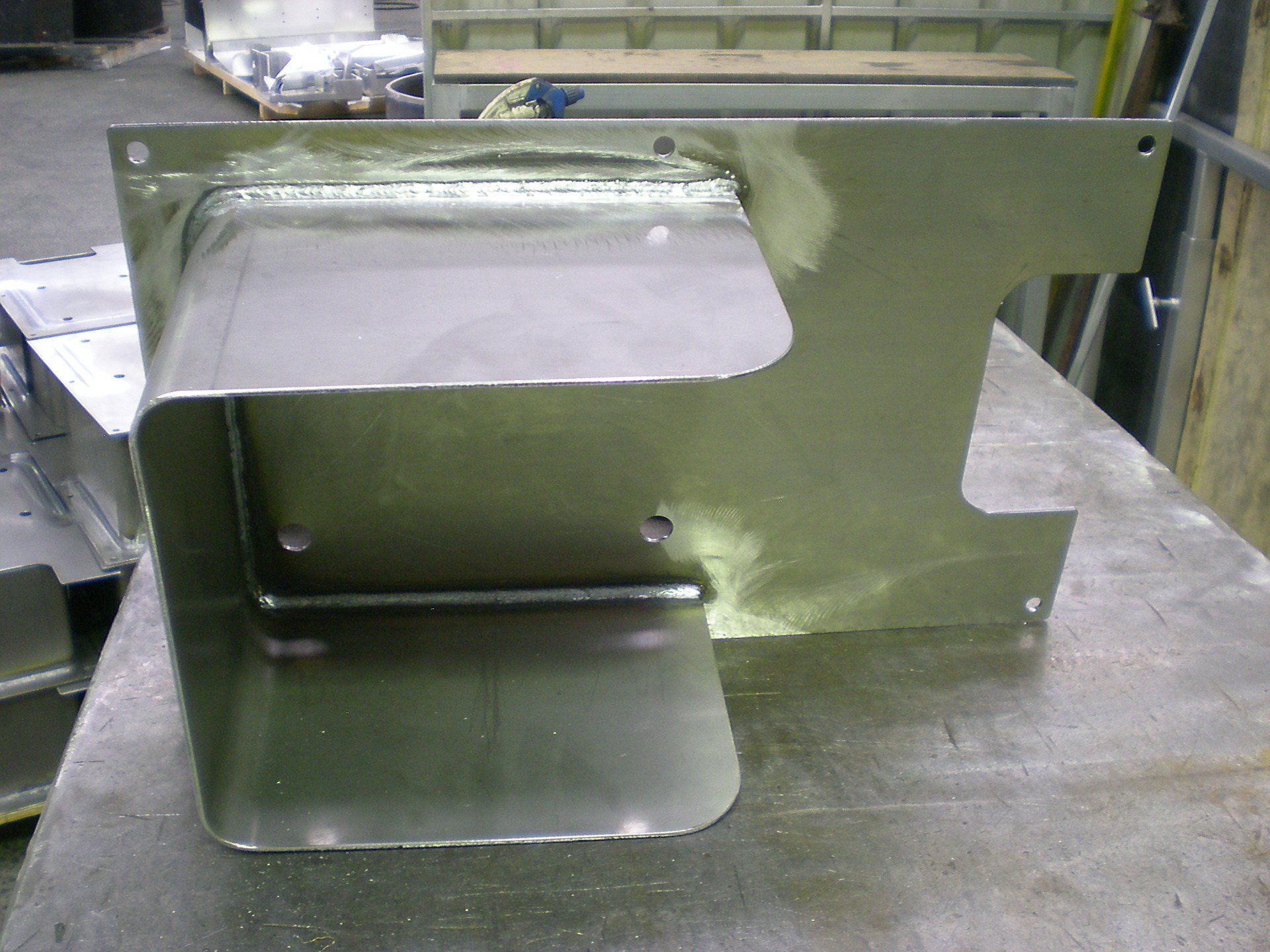 Metal fabricated component on a work surface. It has a rectangular base with an attached, angled box section.