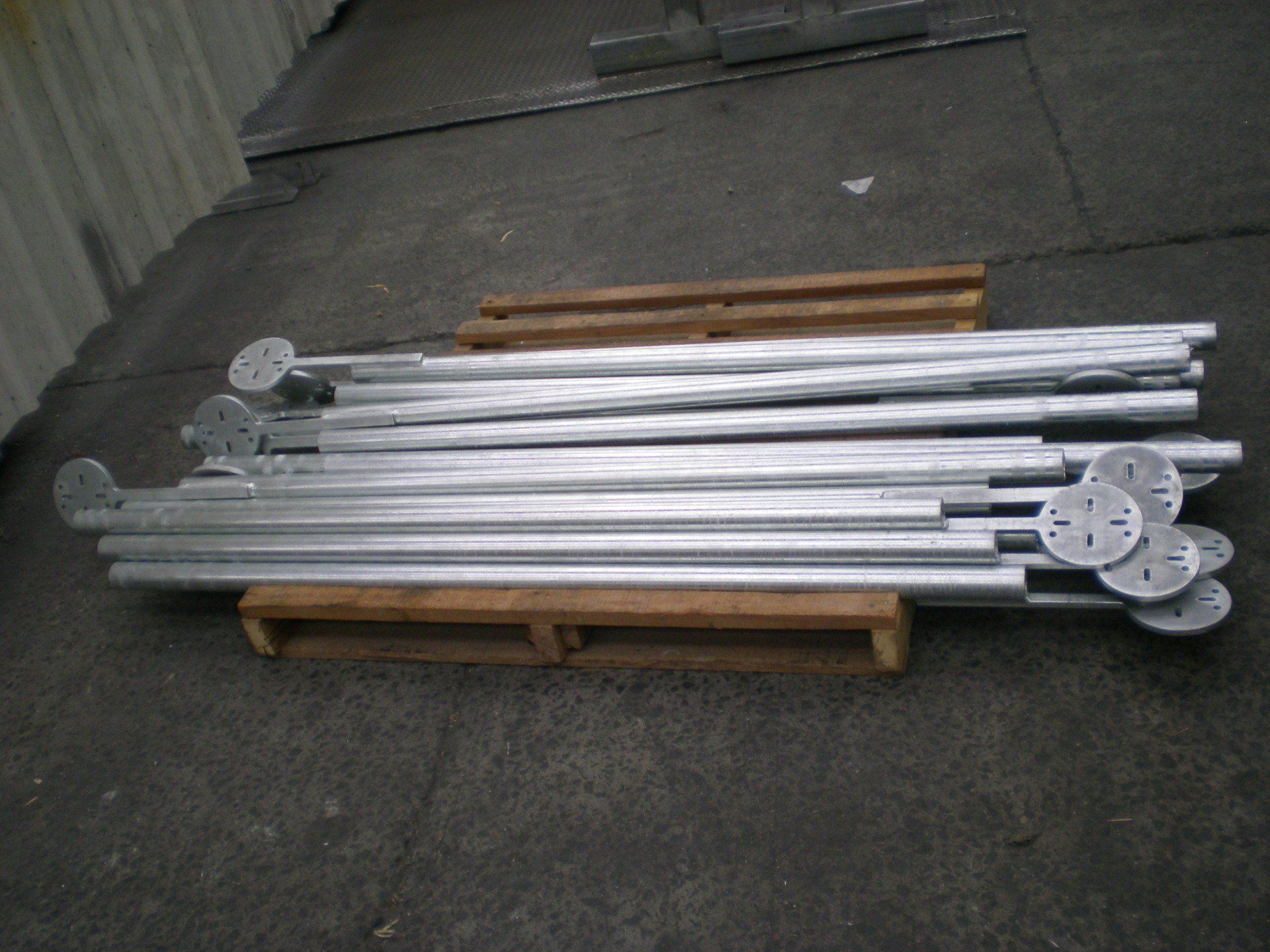 A pile of silver metal poles with circular bases, resting on a wooden pallet in an industrial setting.