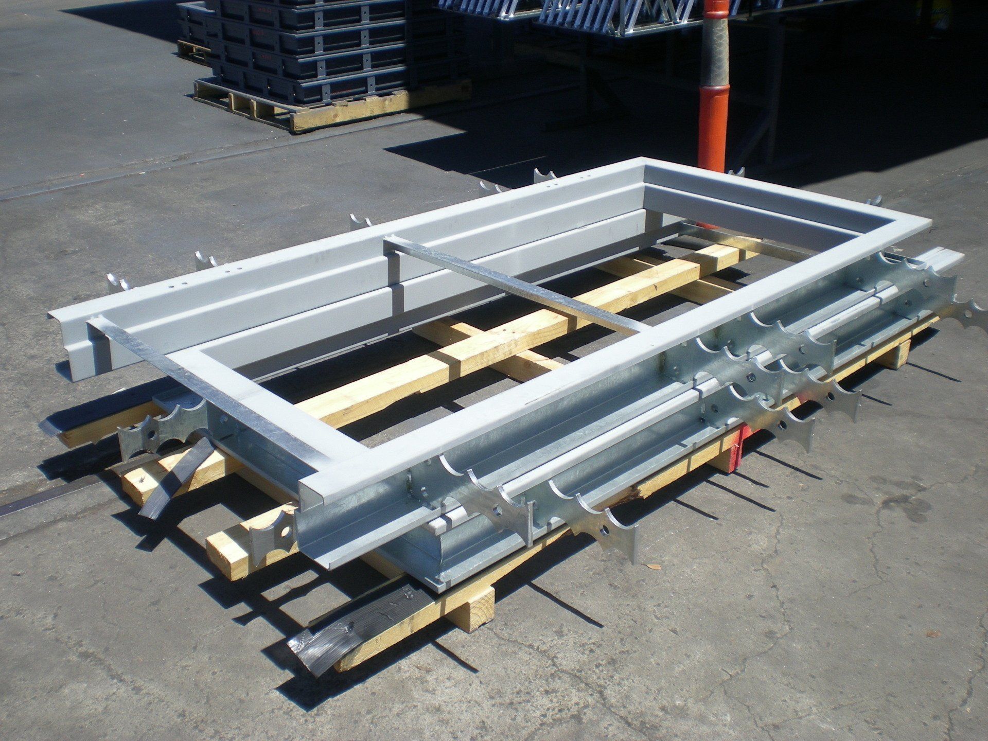 Metal door frame parts, painted gray, stacked on a wooden pallet outdoors.