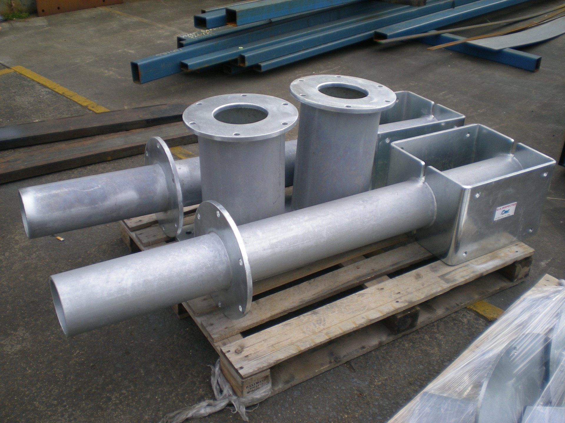 Metal ductwork components on a wooden pallet; includes cylindrical and rectangular sections with circular flanges.