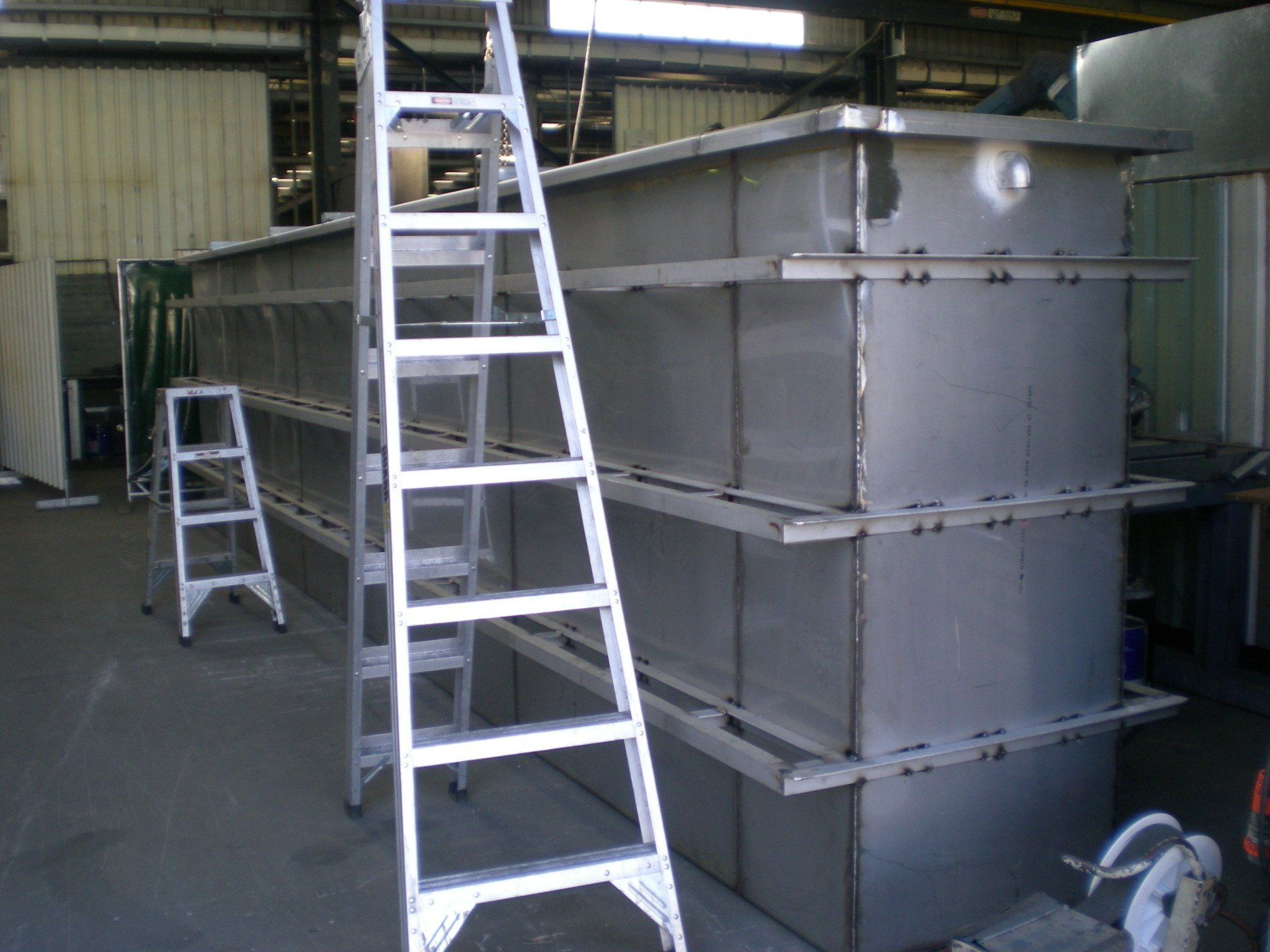 A tall, metal tank structure in a workshop setting with a metal ladder for scale.
