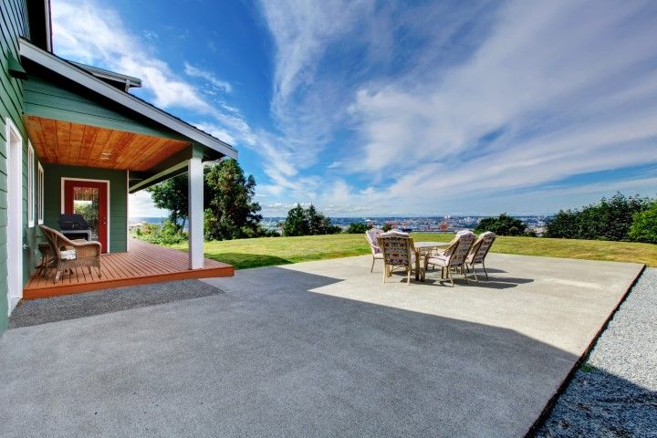 Patio with table and chairs beside a house, overlooking a grassy yard and distant water under a blue sky