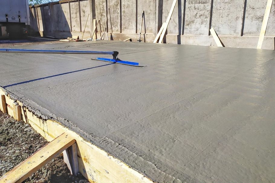 Freshly poured concrete slab at a construction site with blue leveling tools on top
