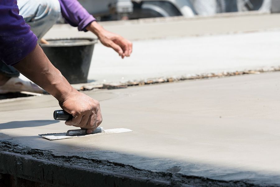 Worker smoothing wet concrete with a hand trowel on a construction site