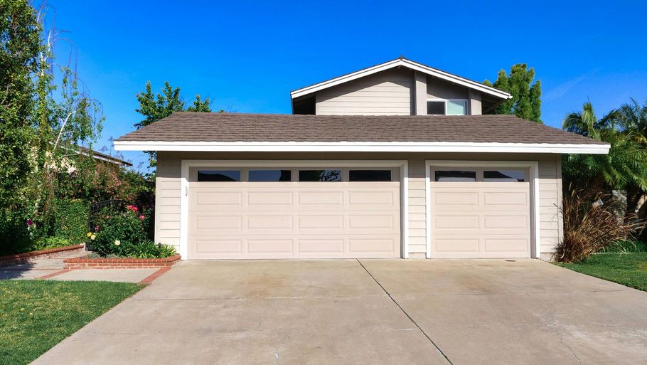 Suburban two-story house with a three-car garage and large concrete driveway under a clear blue sky