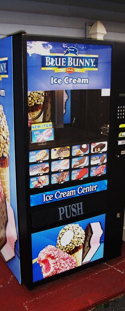 Blue Bunny ice cream vending machine with product images and a push button in a store.