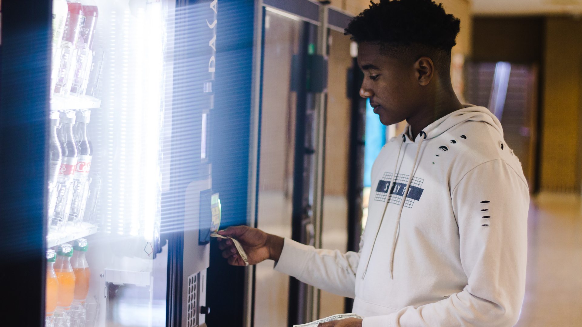 Person in a white hoodie using a vending machine in a bright indoor setting.