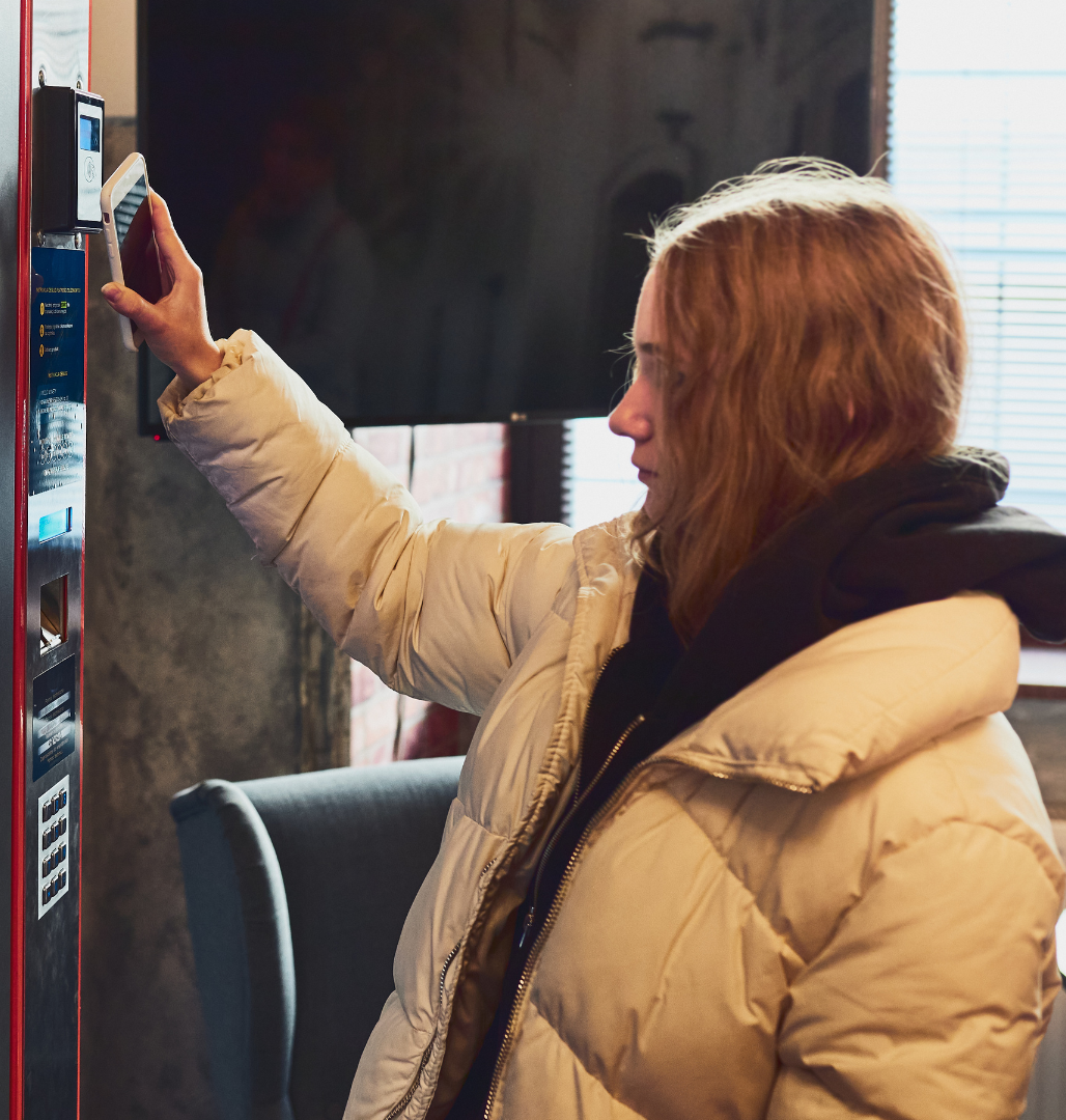 Person in a white puffer jacket reaching toward a refrigerator door in a store or café