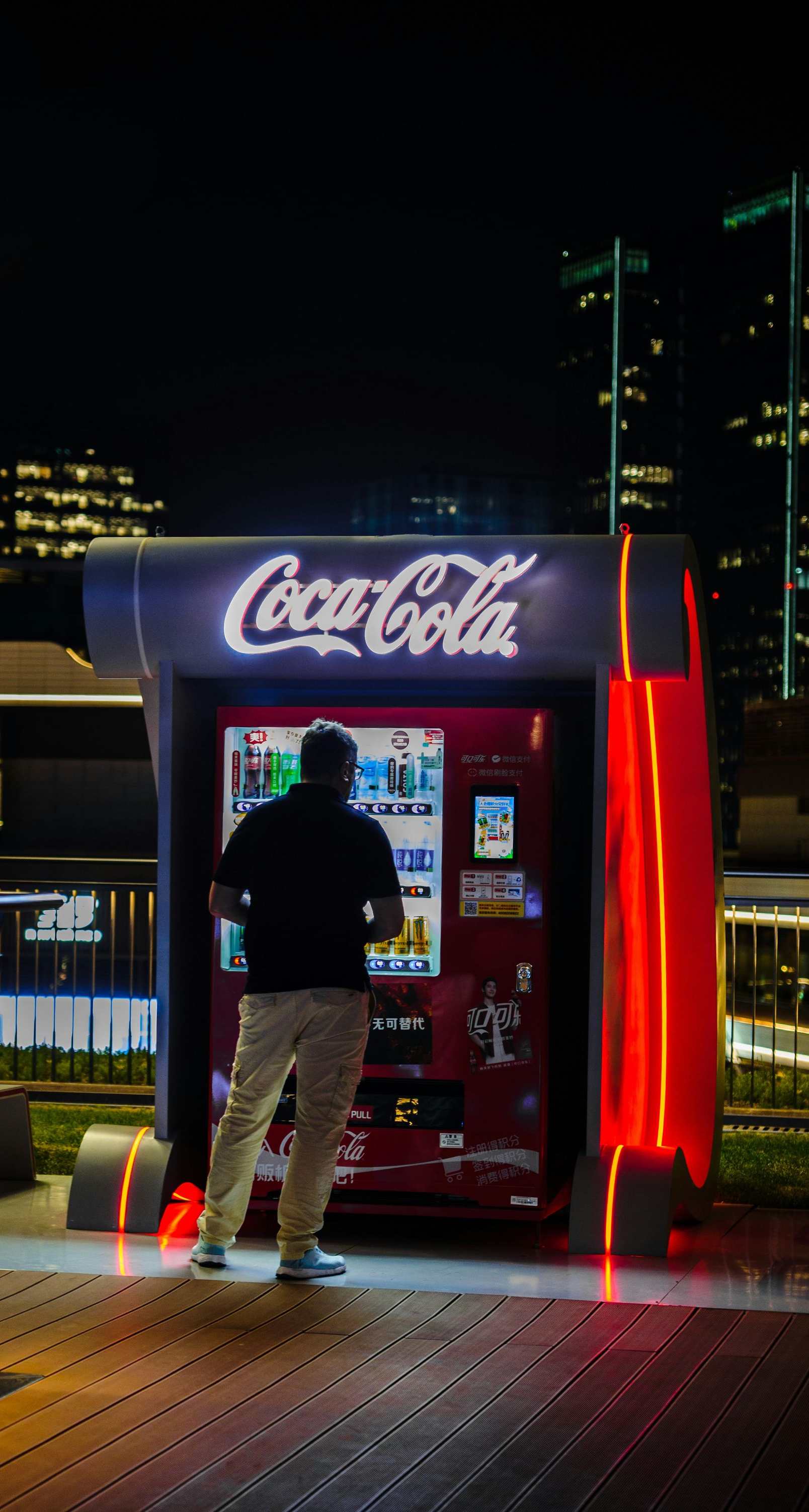 Person using a Coca-Cola vending machine at night on a city overlook deck