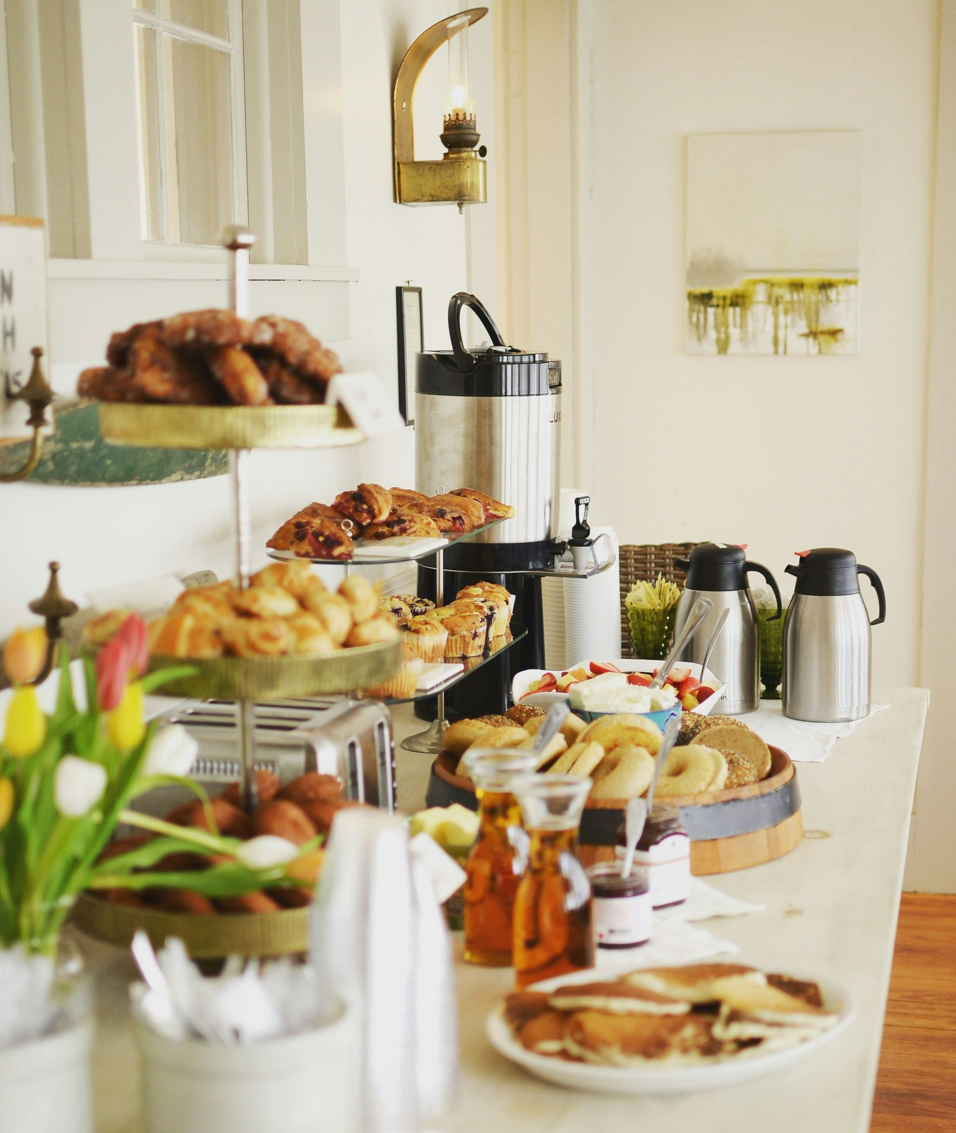 Buffet table with pastries, fruit, coffee pots, and sandwiches in a bright dining room