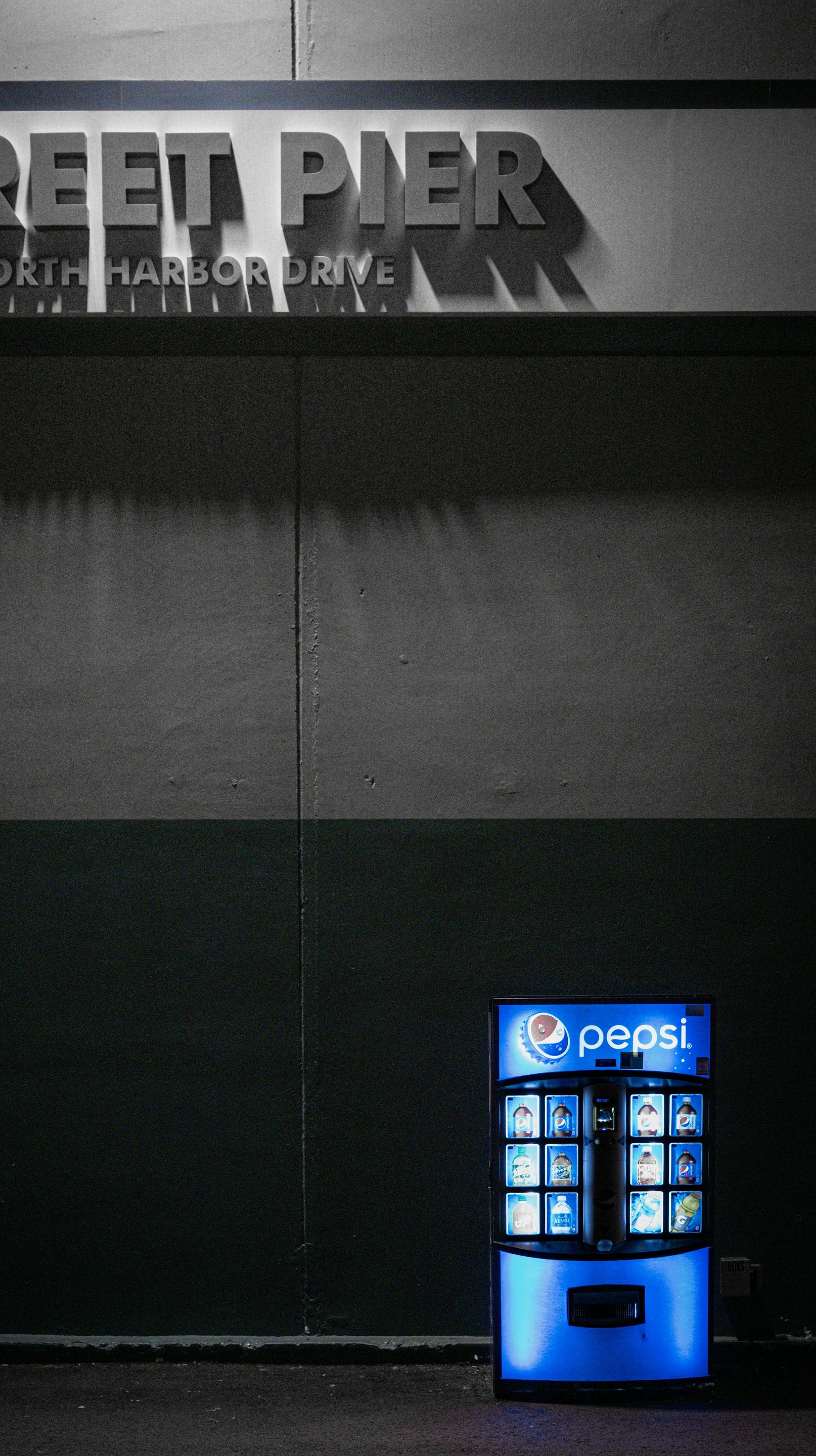 Blue Pepsi vending machine against a dark wall beneath a STREET PIER sign at night