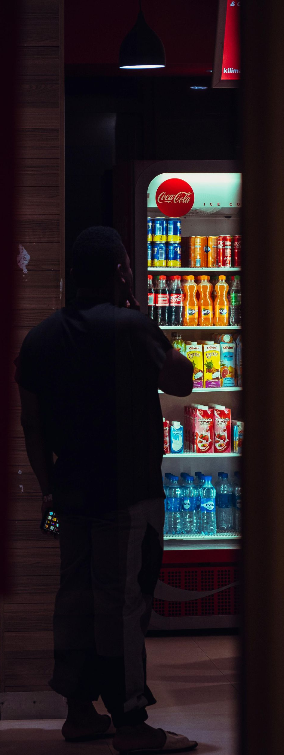 Person standing by a brightly lit vending machine in a dim hallway.