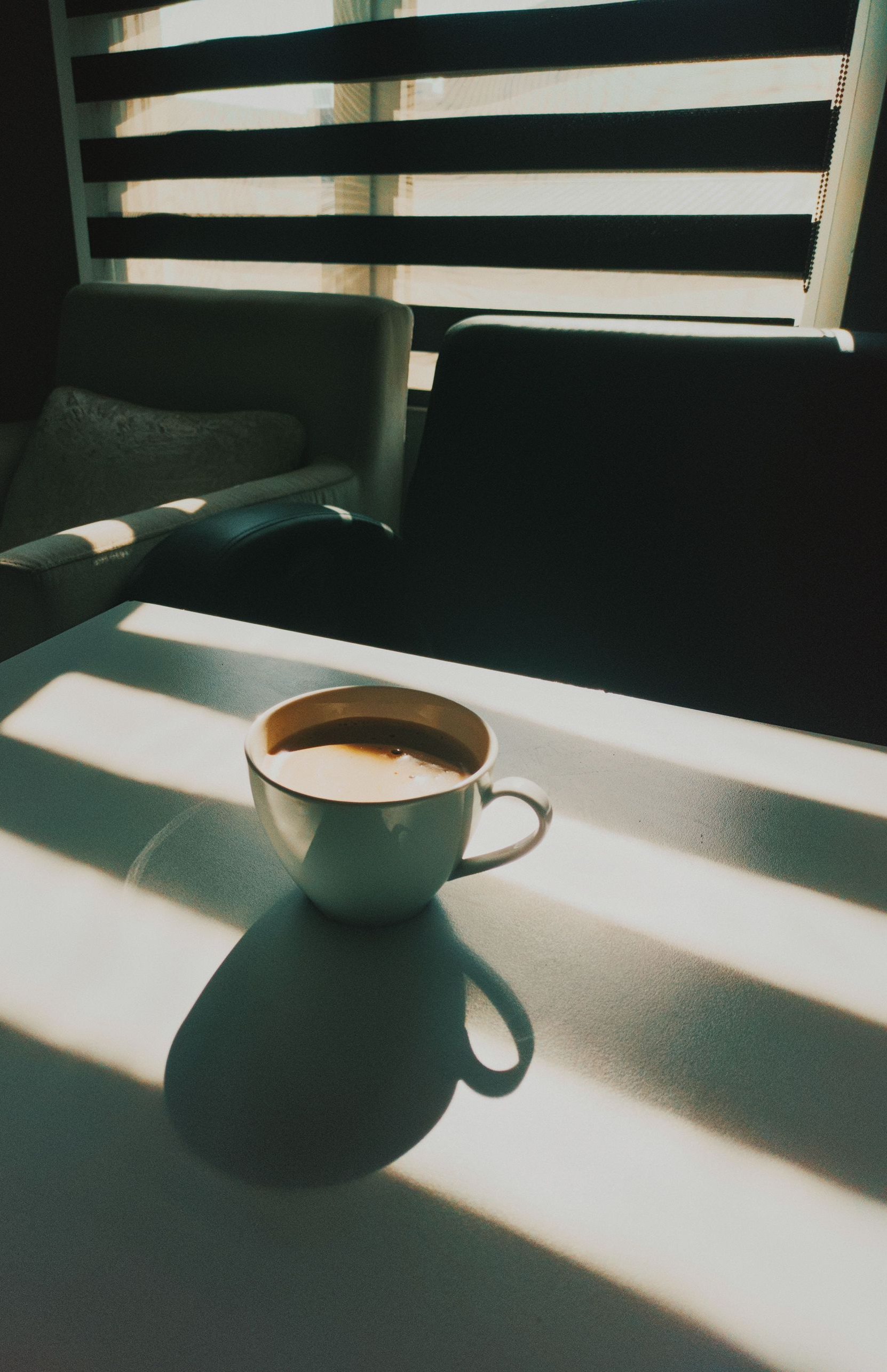 White coffee cup on a sunlit table with striped shadows in a modern room