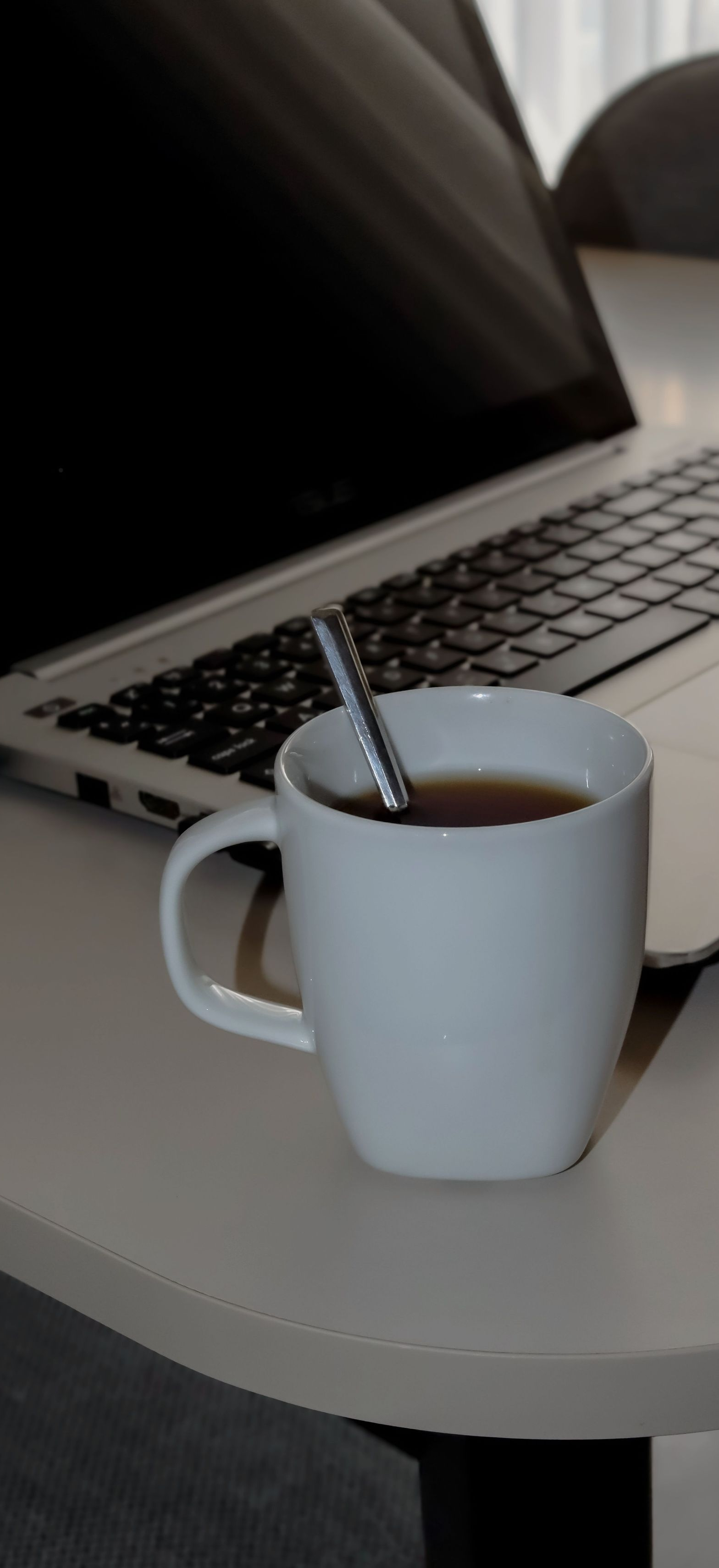 White mug with a spoon on a round table beside an open laptop, likely a coffee break setup
