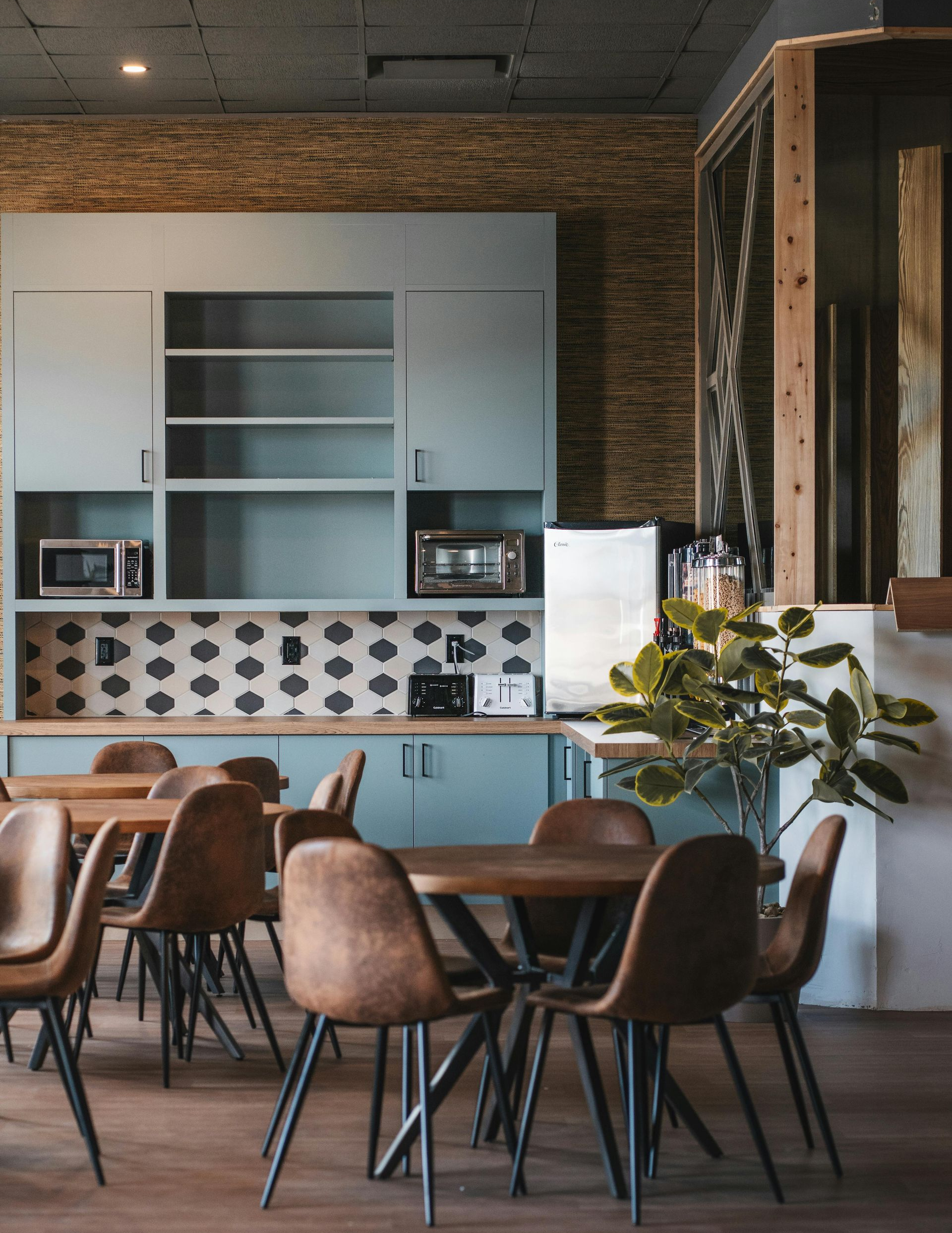 Cozy café interior with wooden tables, brown chairs, and a blue counter with shelving and lamps.