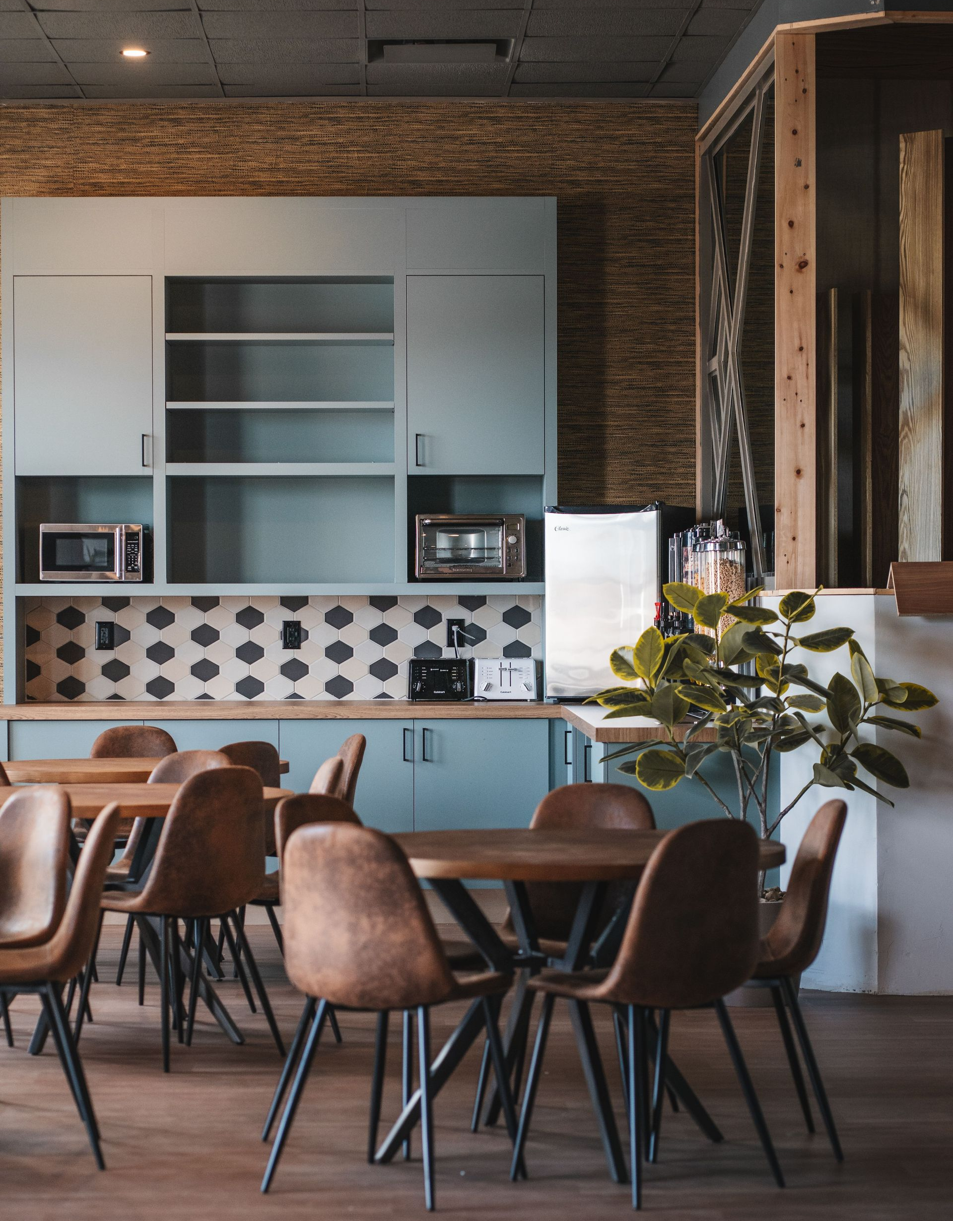 Modern café interior with blue cabinets, brick wall, round wooden tables, and brown chairs