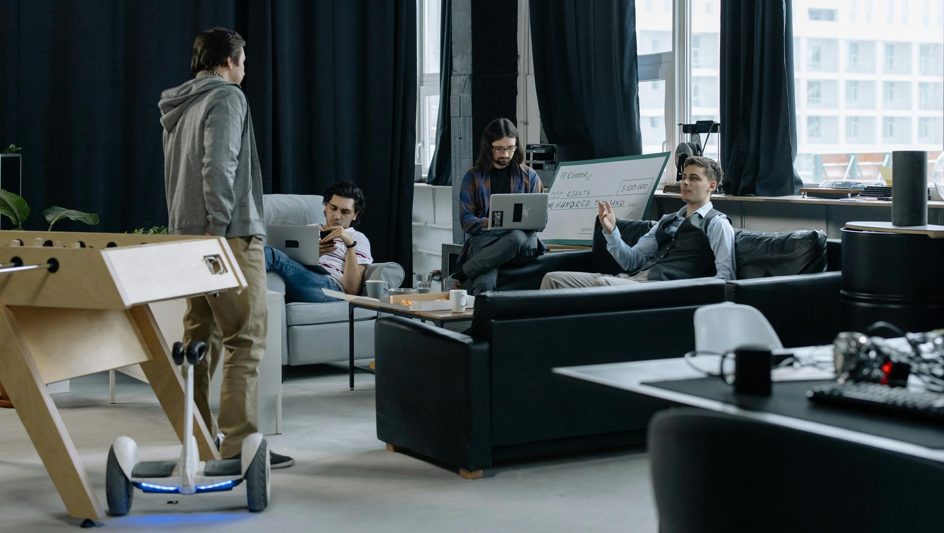 People collaborating in a modern office lounge with sofas, computers, and large windows