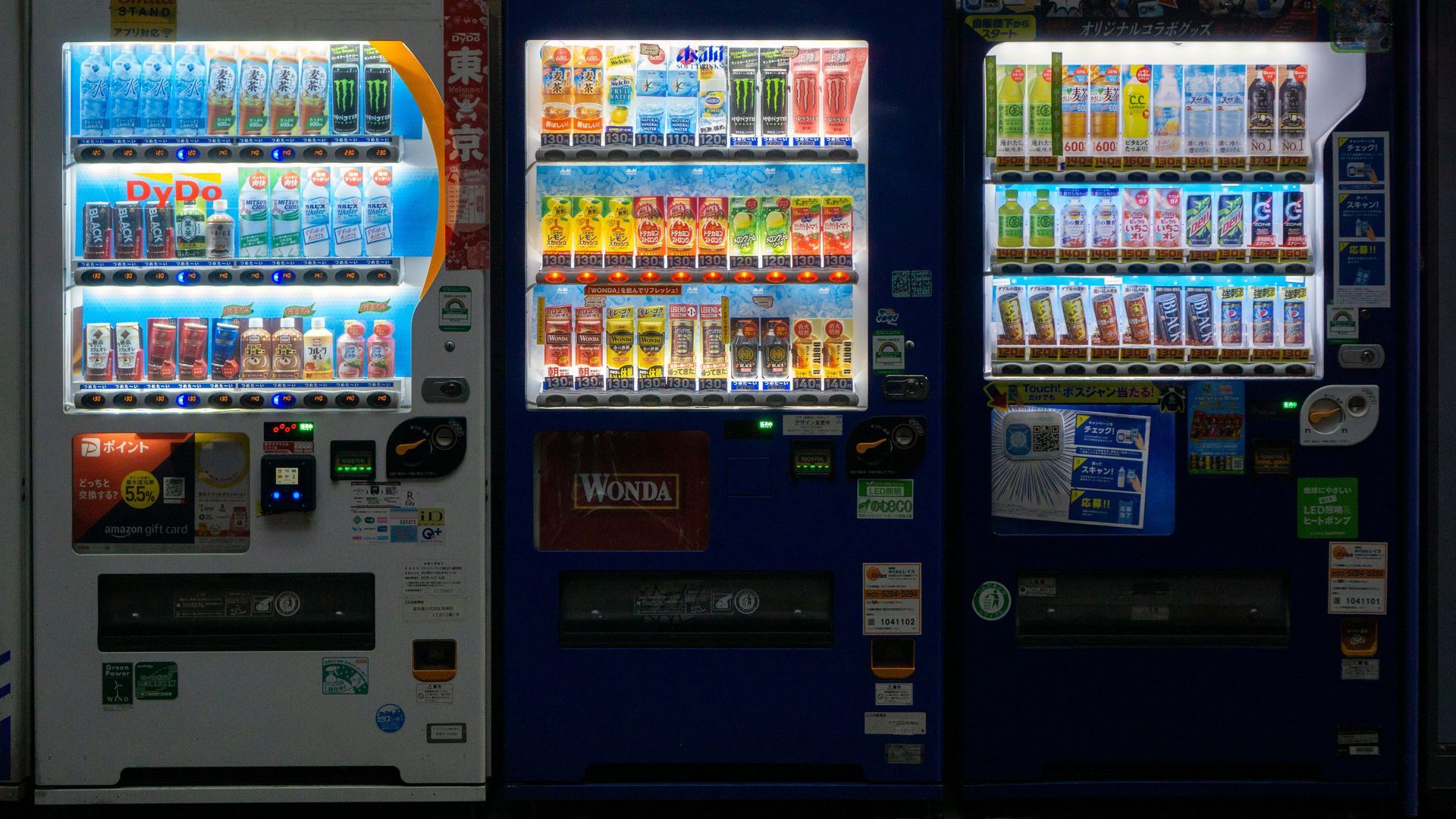 Three illuminated vending machines lined up indoors, stocked with drinks and snacks.
