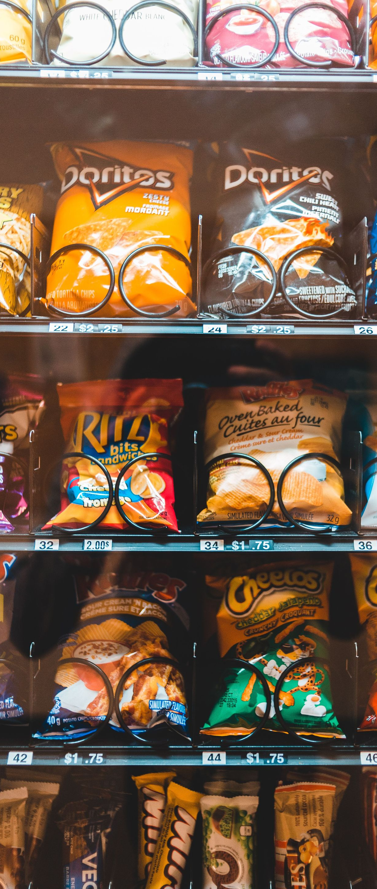 Store shelf stocked with colorful Doritos bags and other chip bags behind glass.