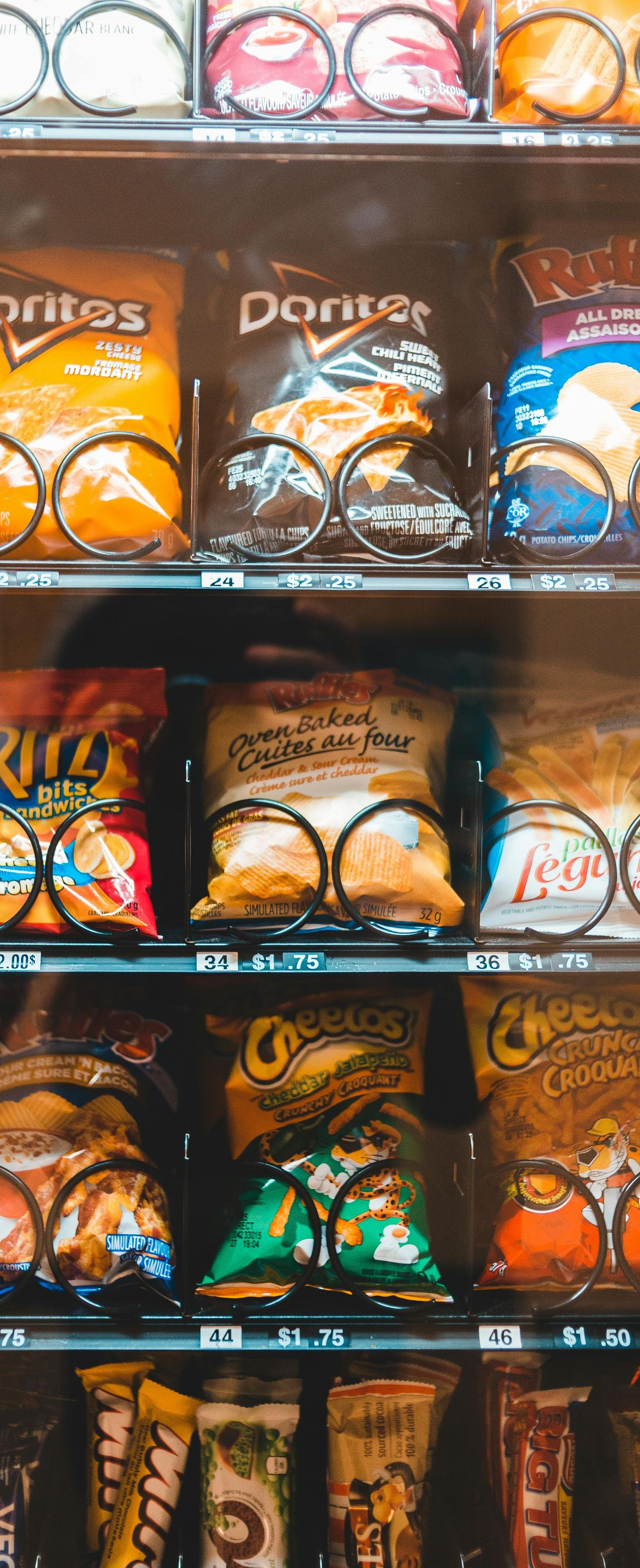 Vending machine shelves filled with assorted snack bags, mostly chips and chips-like treats in colorful packaging