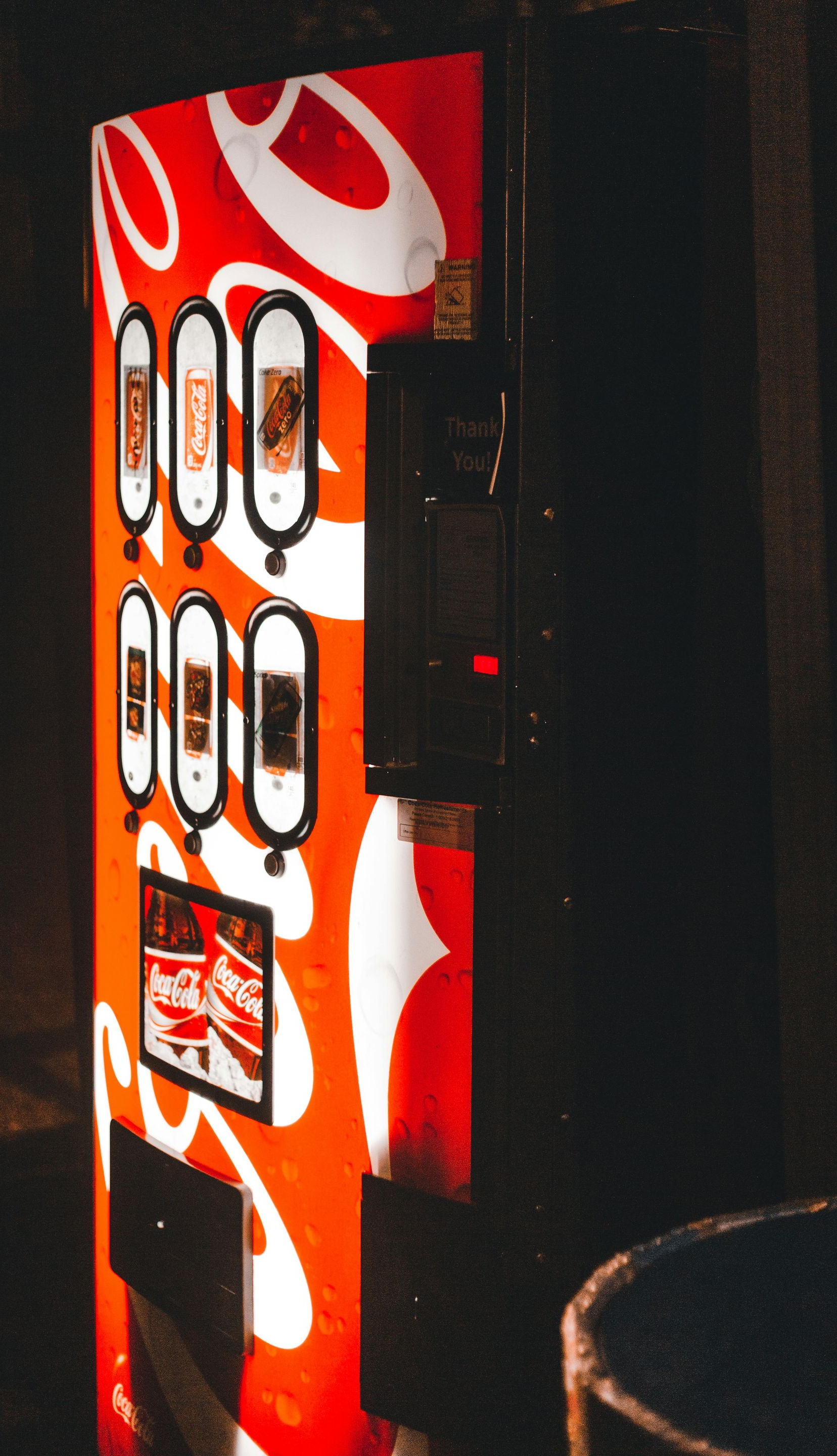 Red vending machine with white swirl design in a dark room, beside a round table.