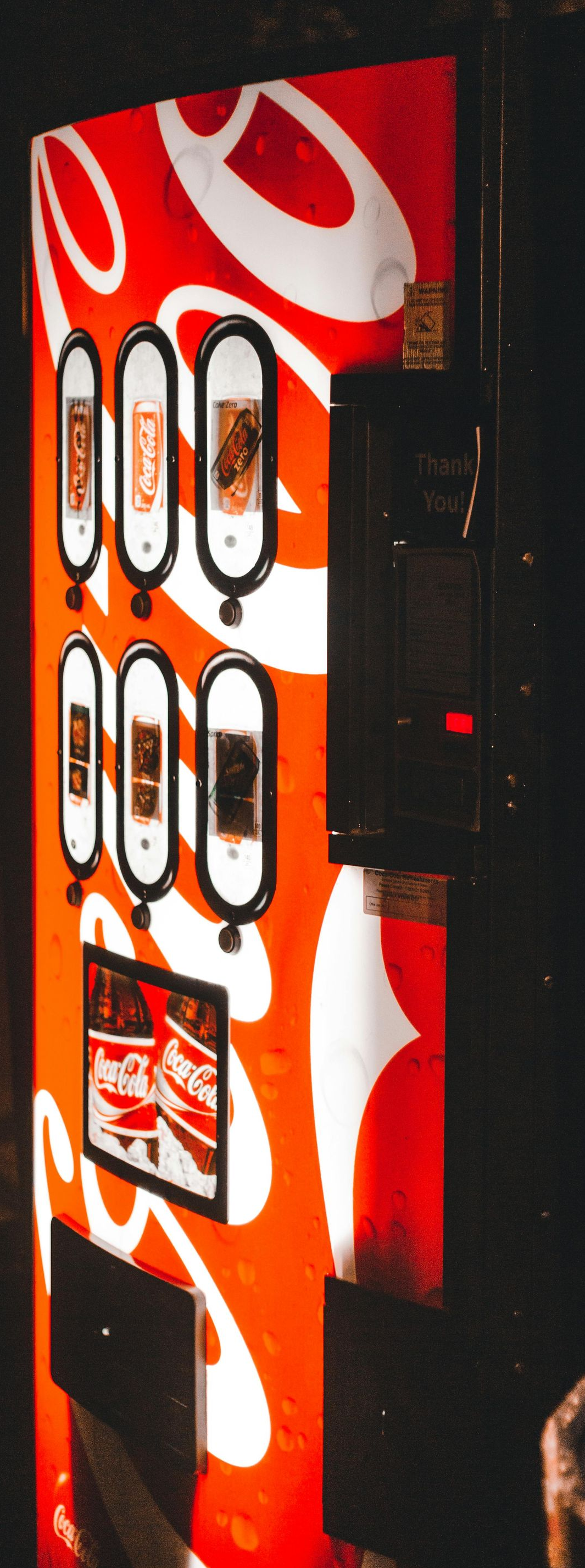 Red vending machine with white swirl design in a dark room, beside a round table.