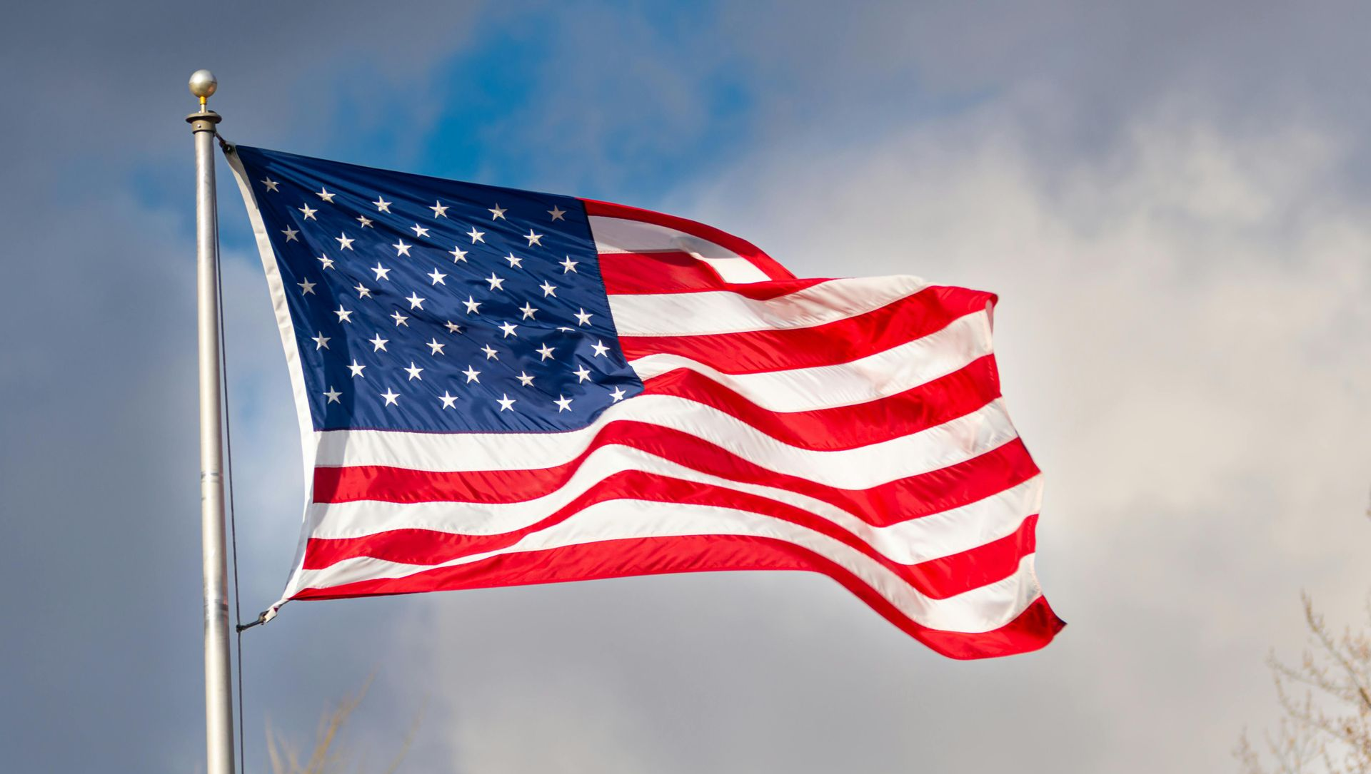 American flag waving on a pole against a cloudy sky