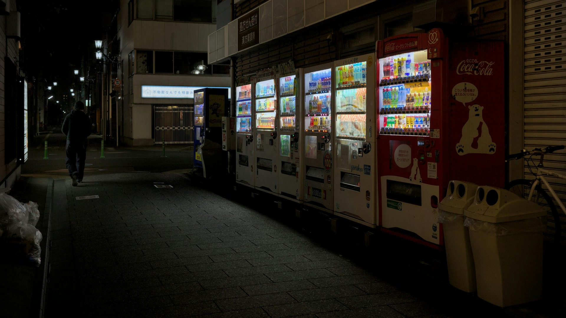 Dim street with brightly lit vending machines along a building at night