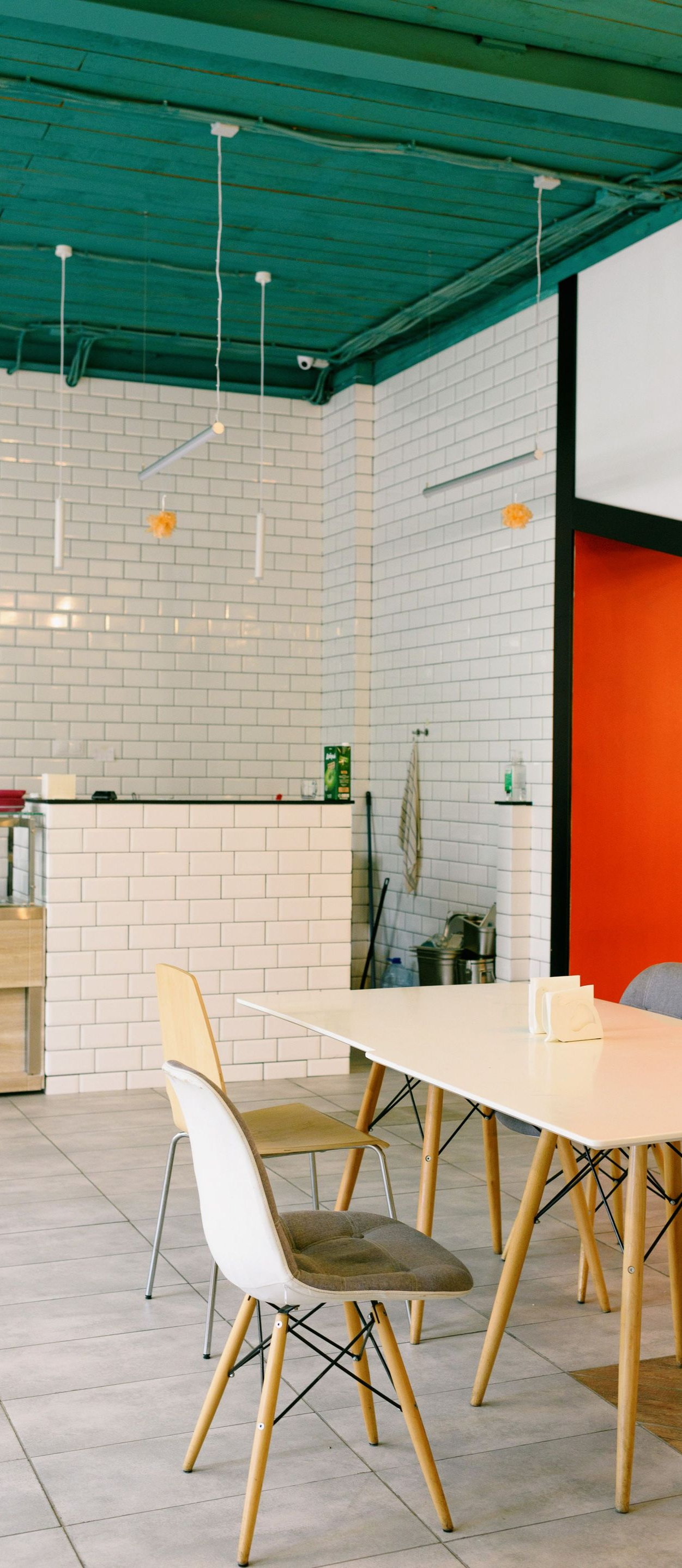 Bright cafe with white tables, wooden chairs, tiled floor, white brick walls, and a teal ceiling.