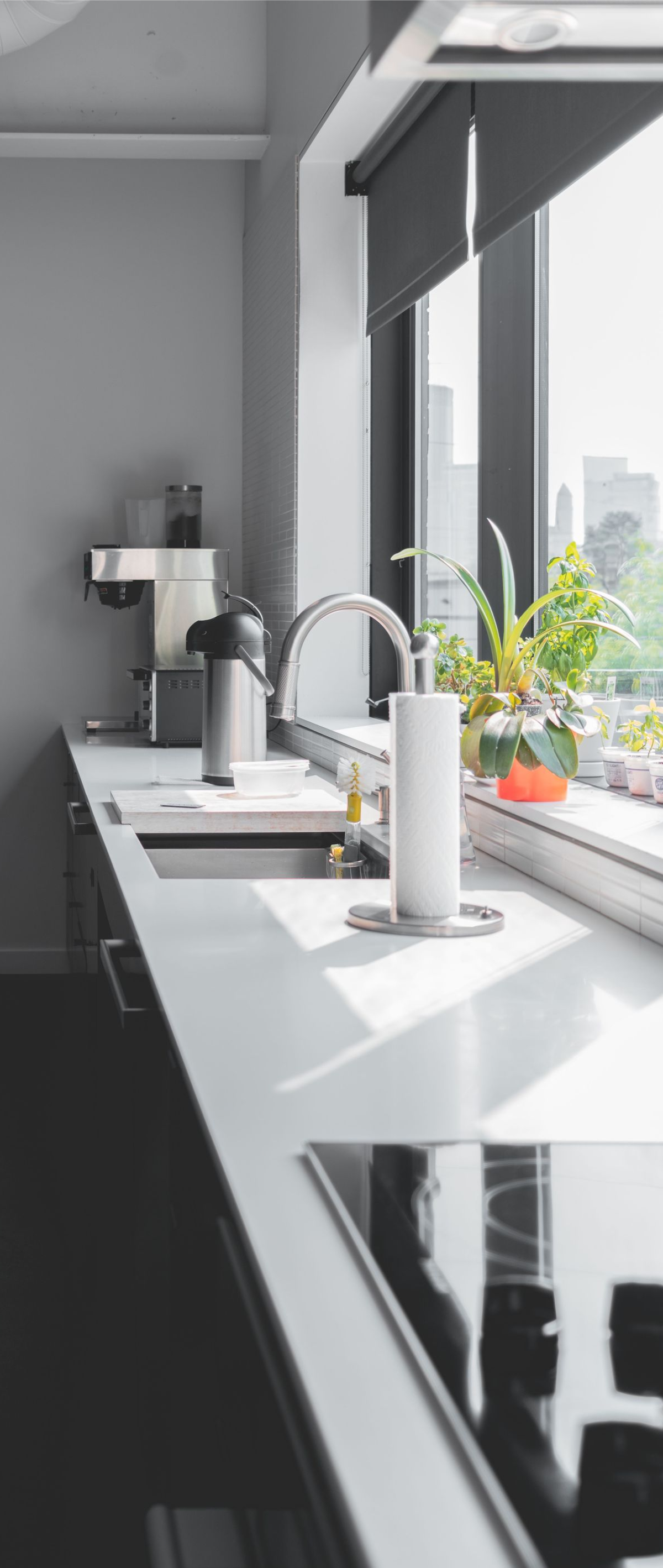Modern kitchen counter by large window with sink, plants, and city view