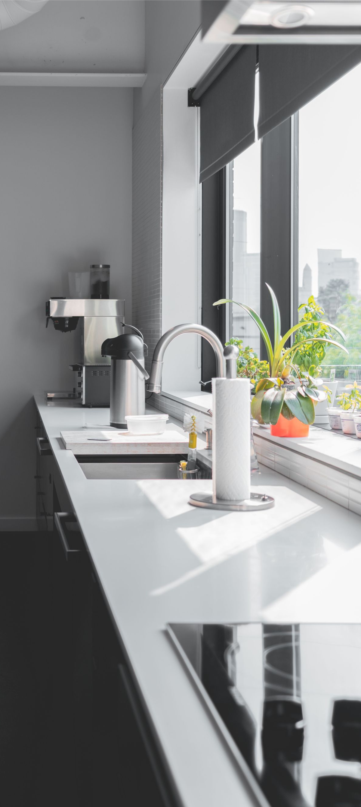 Modern kitchen counter by large window with sink, plants, and city view