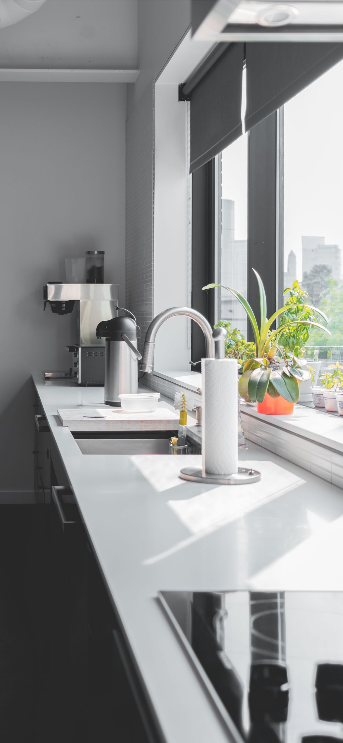 Modern kitchen counter by large window with sink, plants, and city view