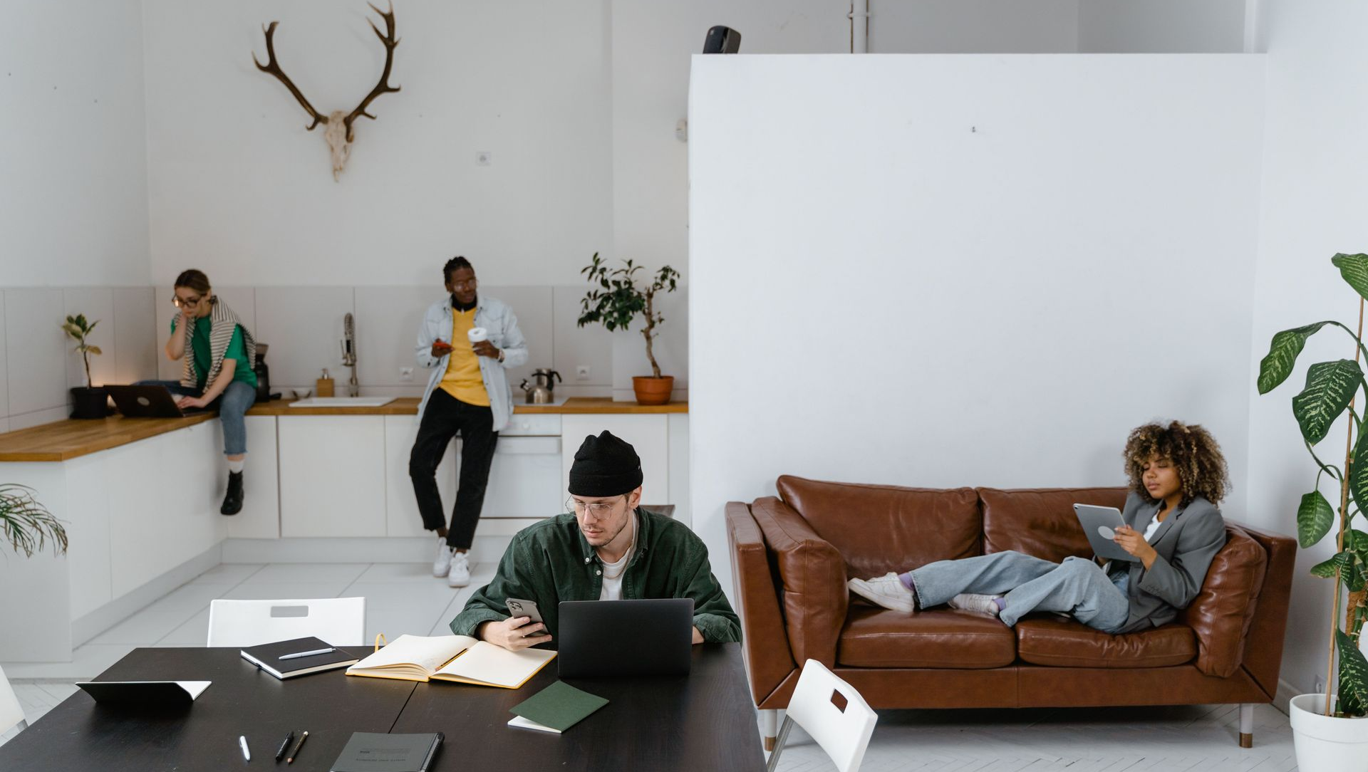 Modern office lounge with people working at desks and one person reclining on a brown sofa.