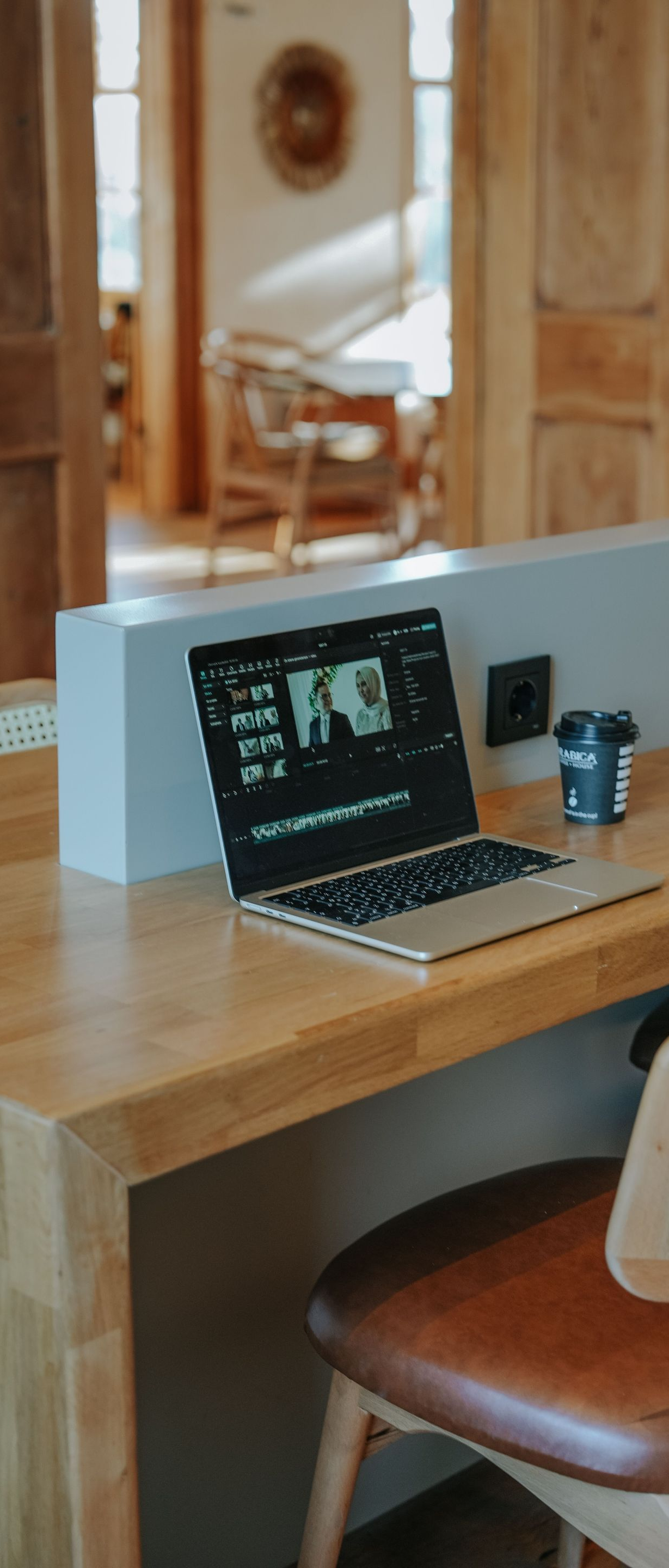 Laptop on a wooden desk by a window, with a coffee cup and chair in a warm home office.