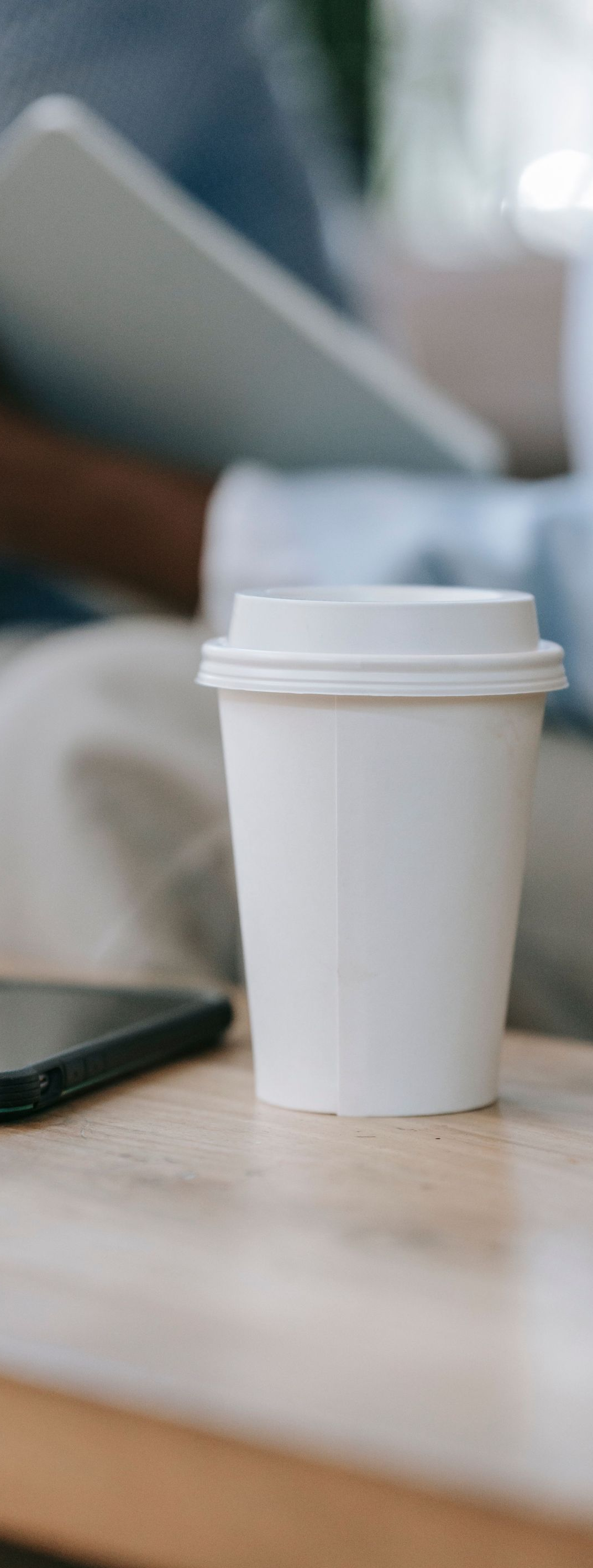 White takeaway coffee cup on a table with a laptop in the background
