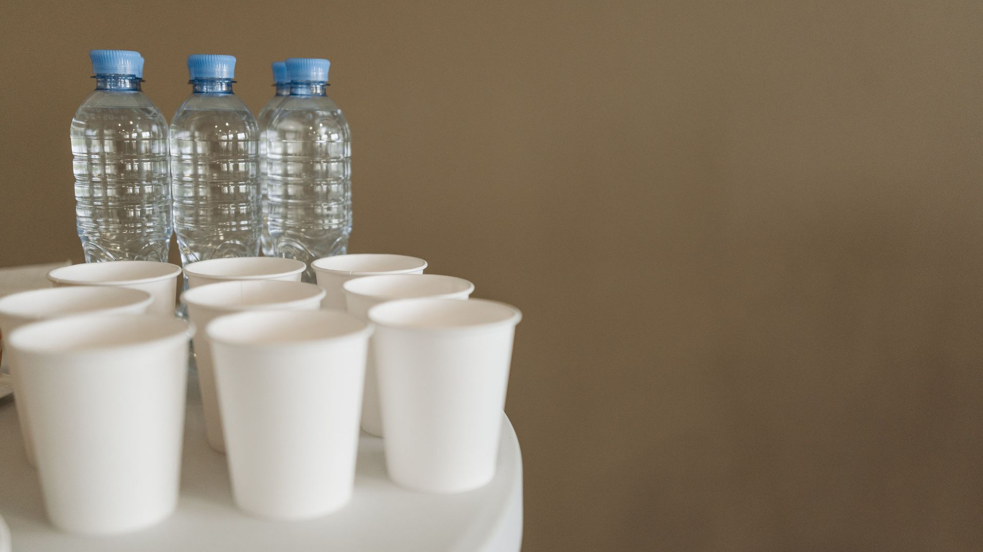 Several white cups and water bottles on a round table against a plain wall