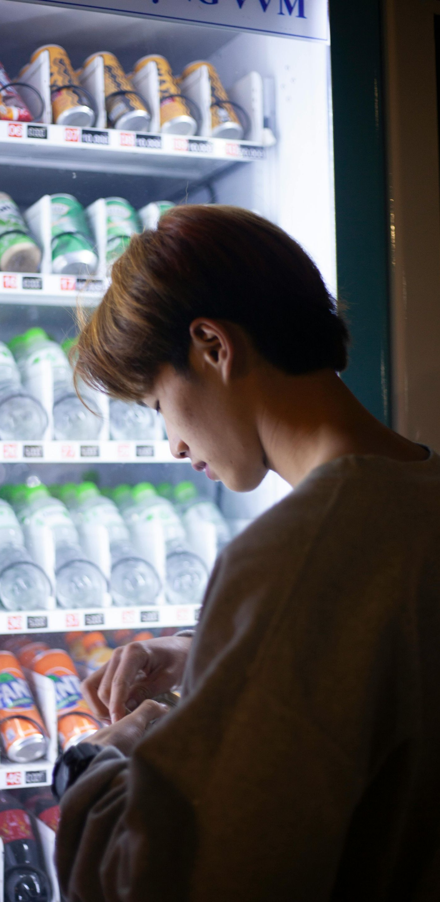 Person standing beside a brightly lit vending machine, looking down at the snack display