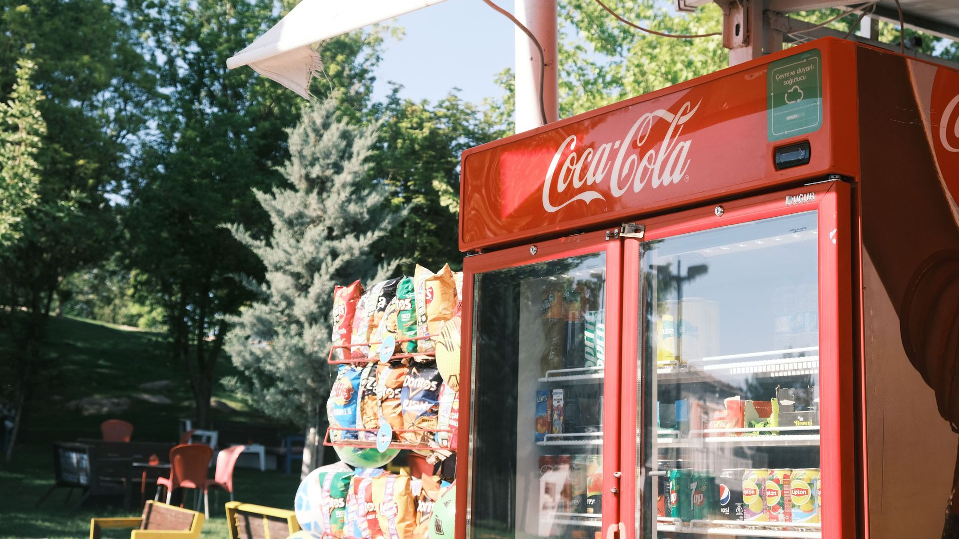 Coca-Cola cooler by a sunny outdoor stand with snacks and trees in the background