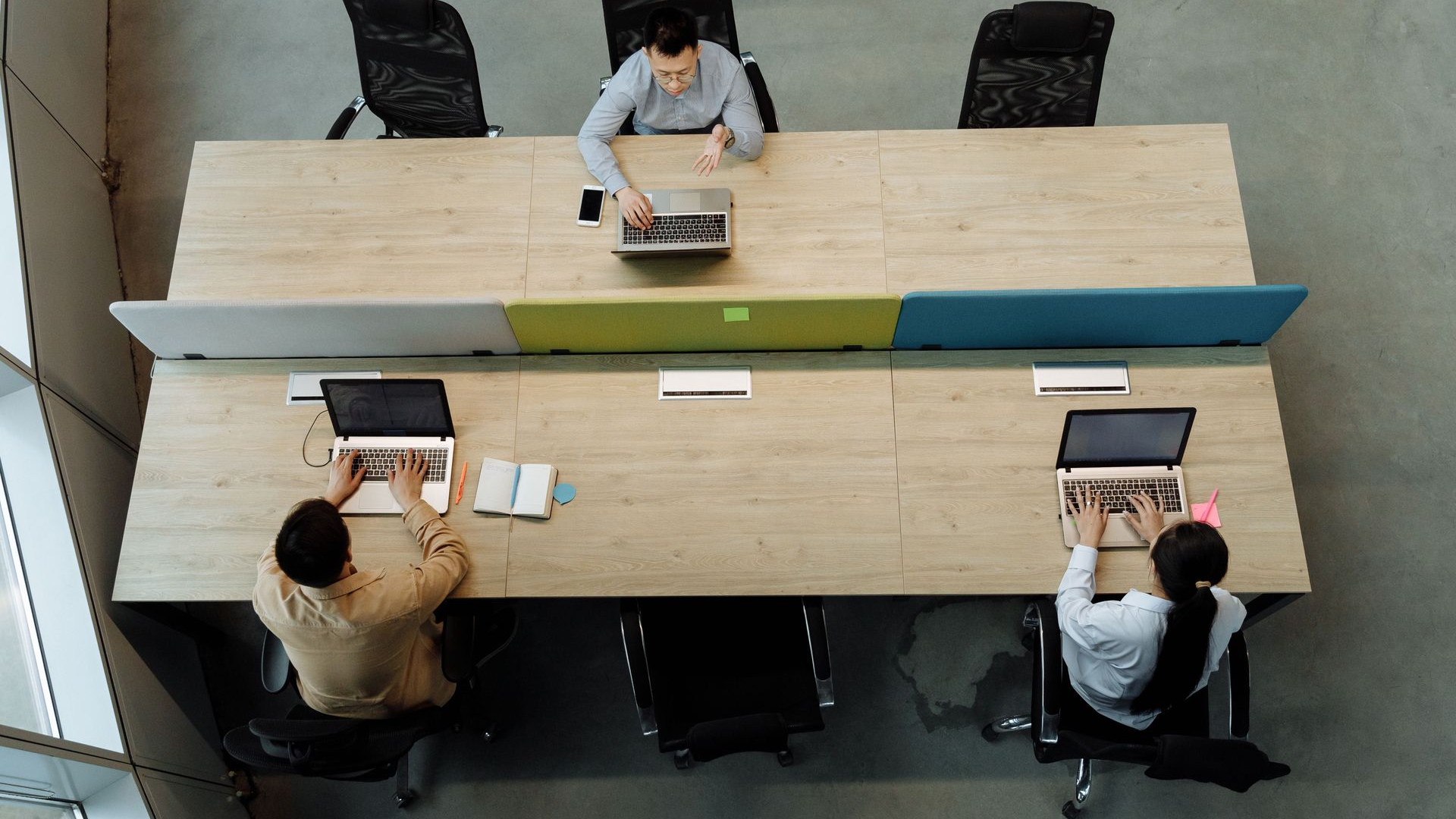 Overhead view of three people working at a long shared table in an office meeting space