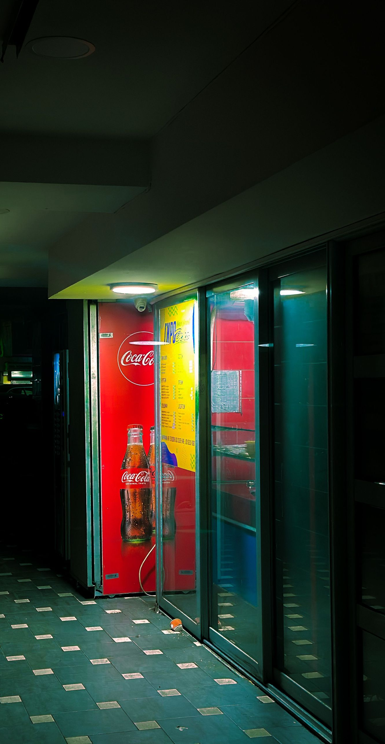 Dim hallway with a bright red vending machine and glass doors on the right side.