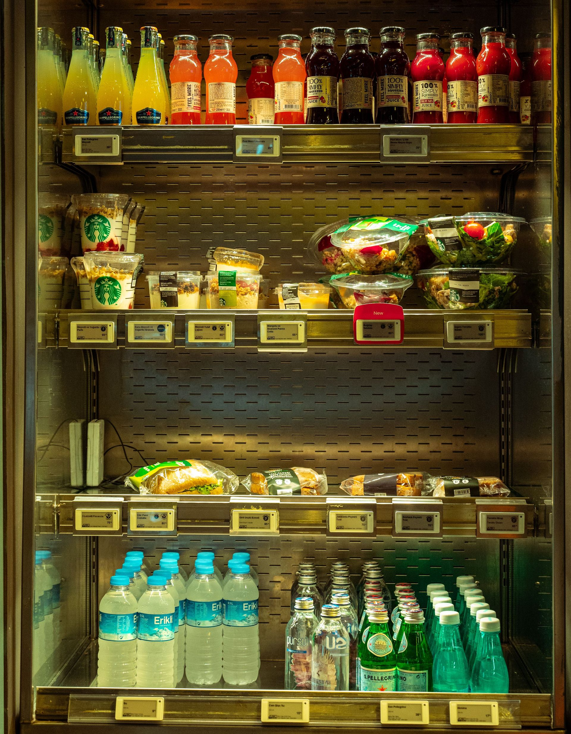 Store beverage cooler stocked with colorful drinks and snacks on metal shelves.