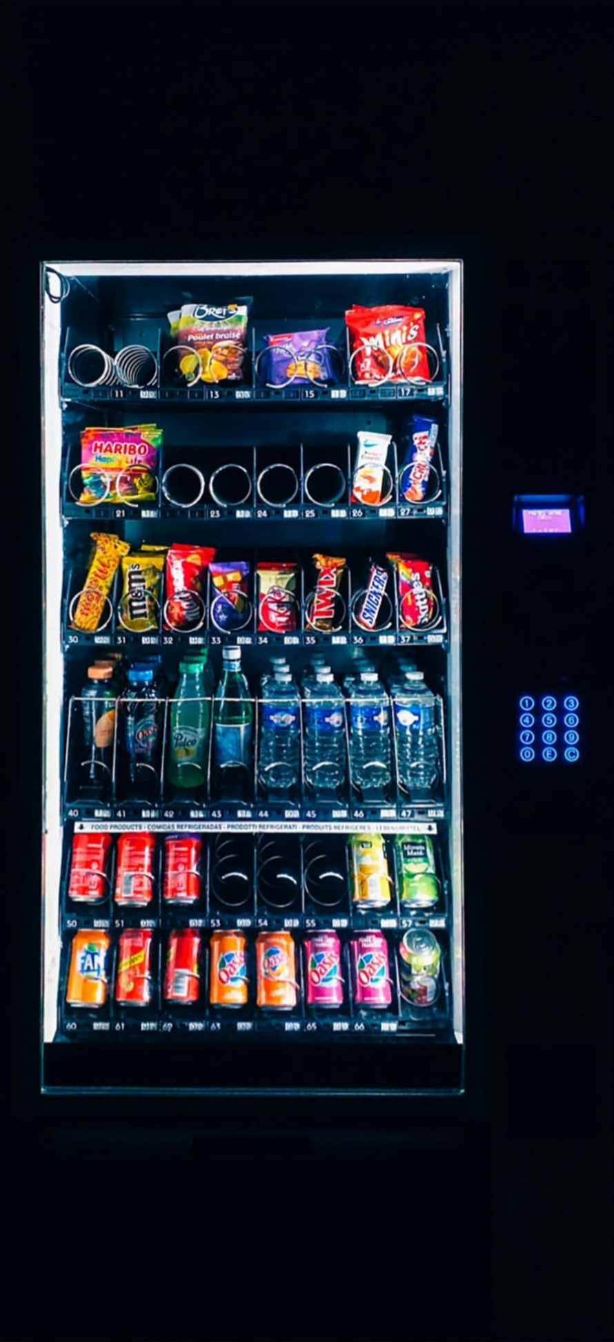 Illuminated vending machine stocked with assorted snacks and drinks against a dark background